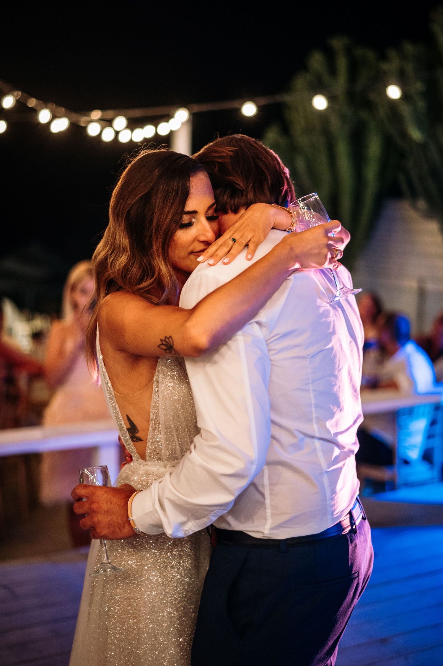 A couple shares an intimate slow dance moment at their wedding reception under twinkling lights.