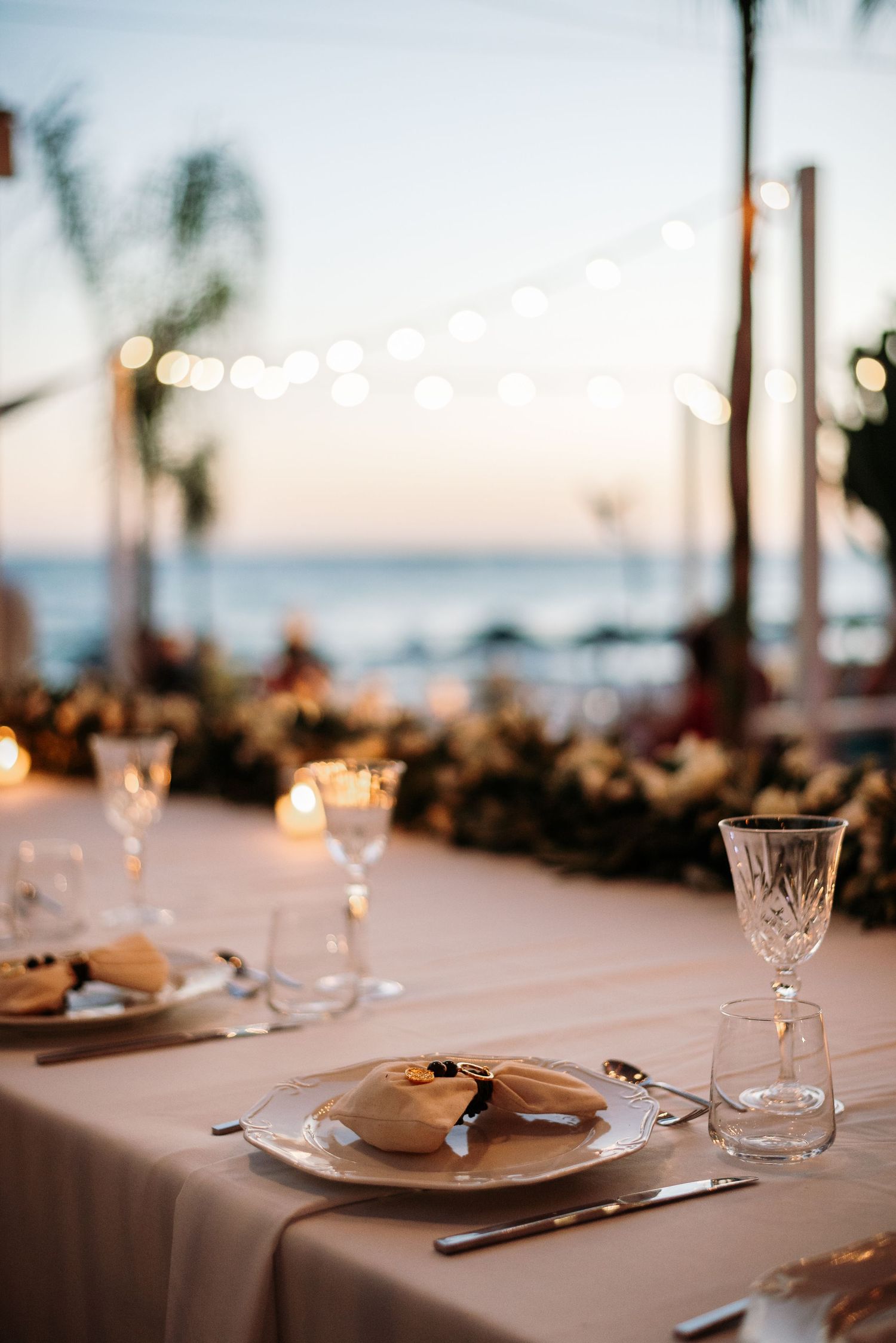 Elegant wedding reception table settings with glassware at sunset by the ocean.