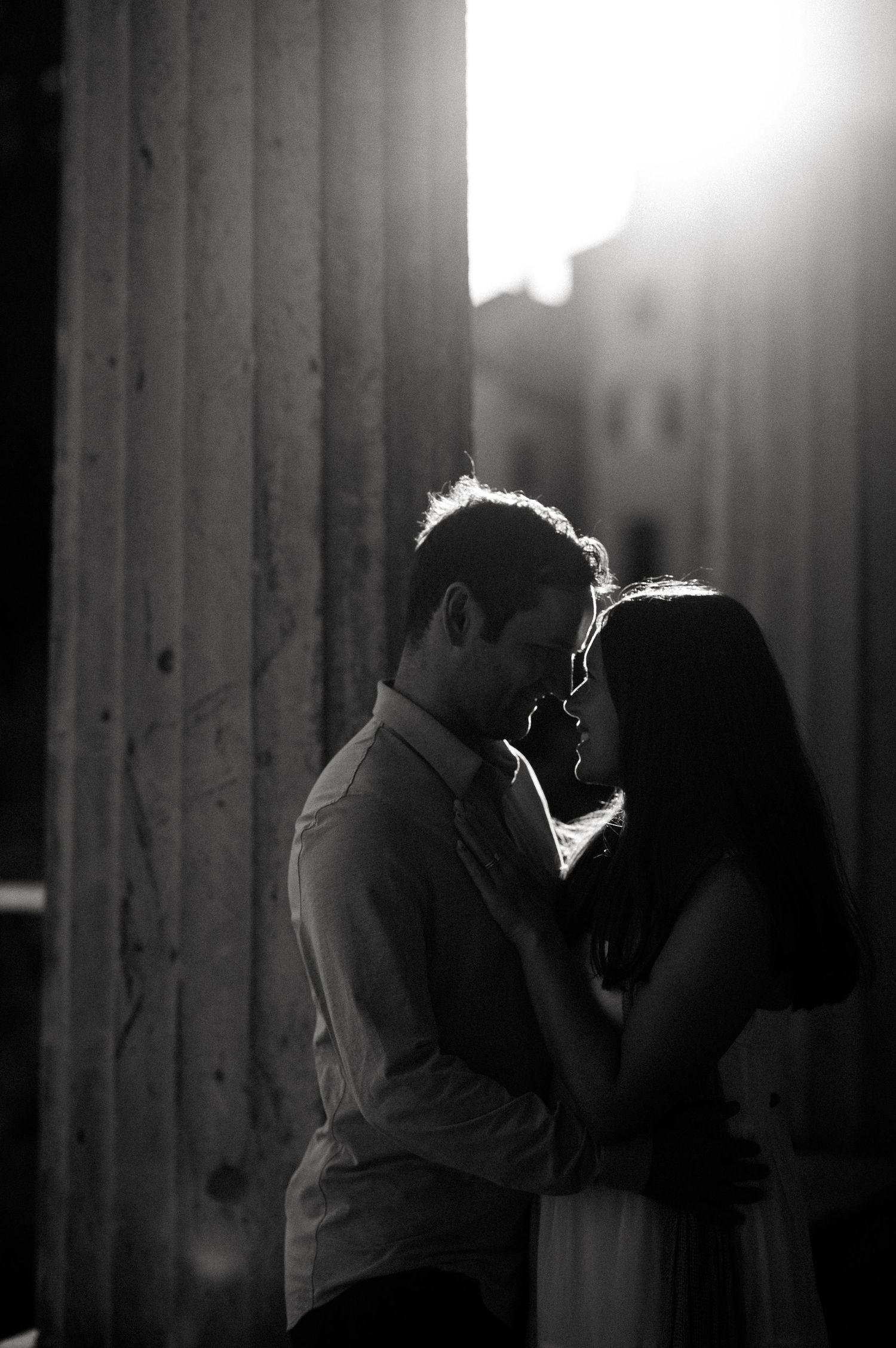 Silhouetted couple sharing an intimate moment in dramatic black and white lighting.