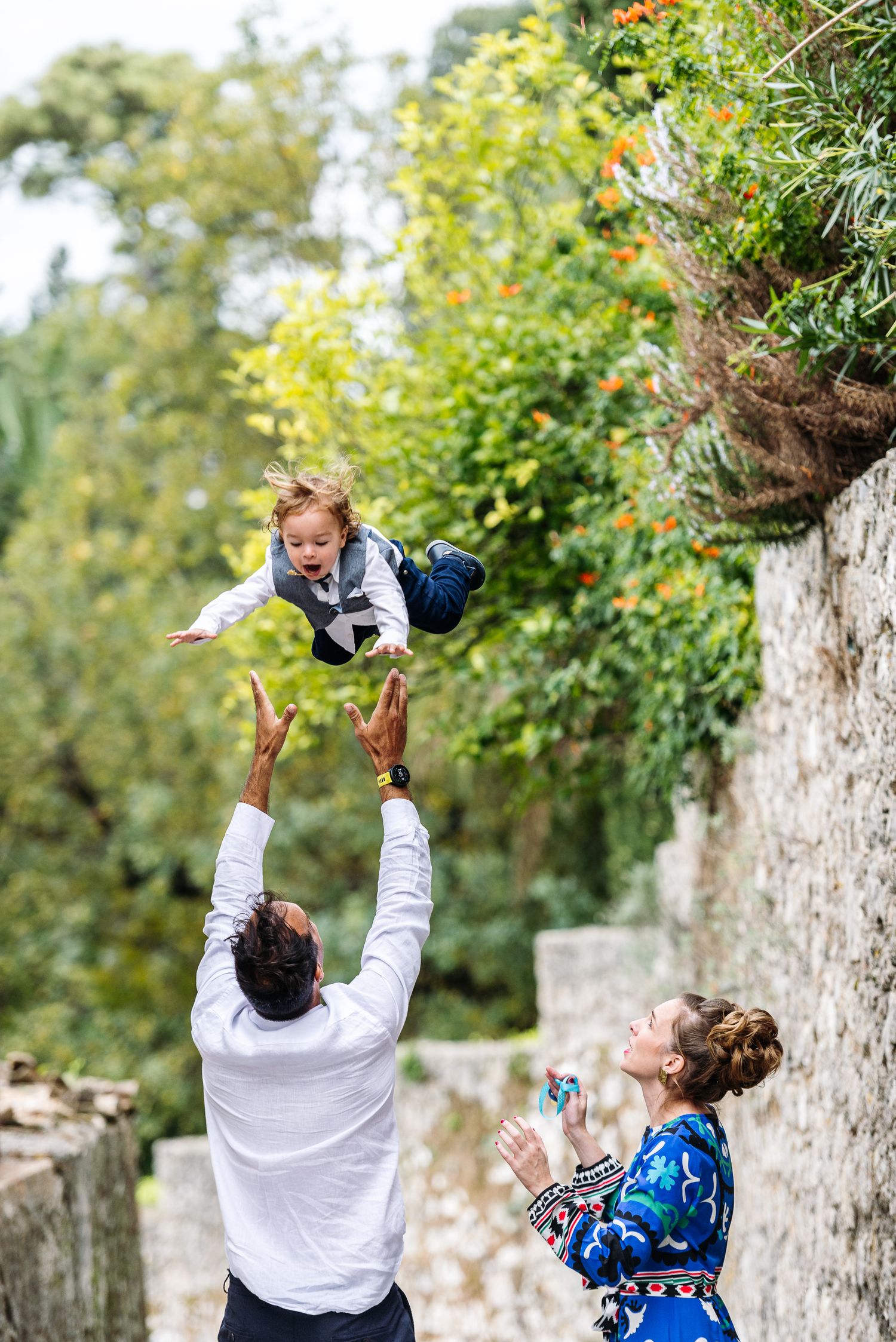 Joyful family moment captured in garden setting with stone wall background.