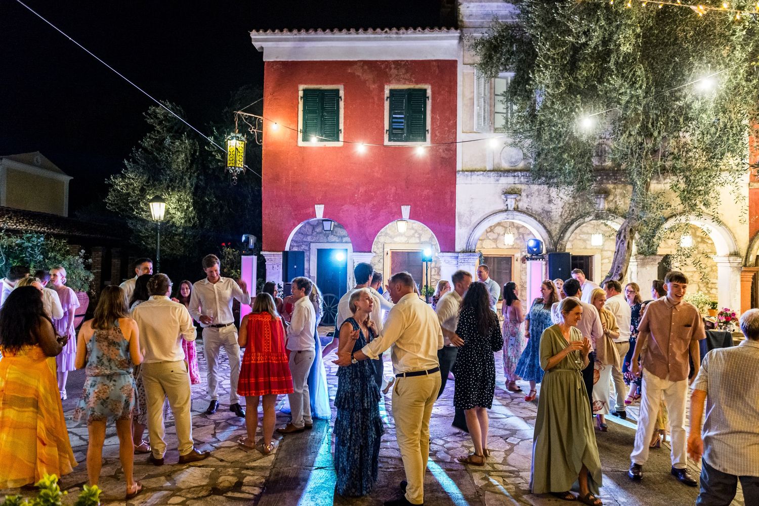Wedding guests in formal attire mingling outdoors under evening lighting and palm trees.