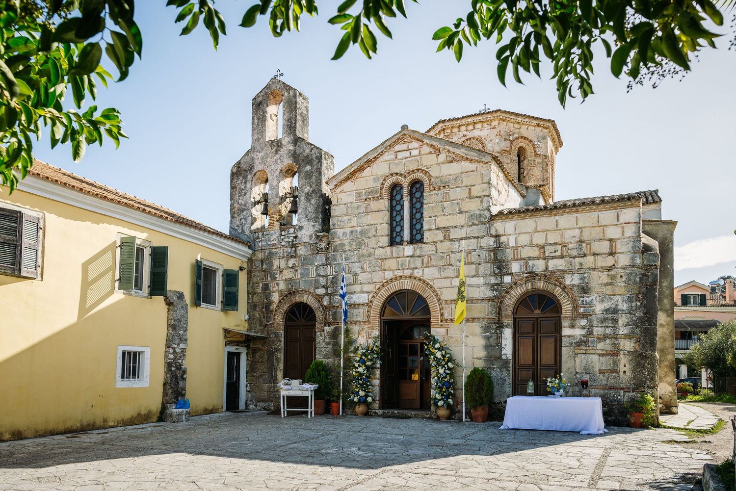 Stone church exterior with arched doorways and green trees overhead.