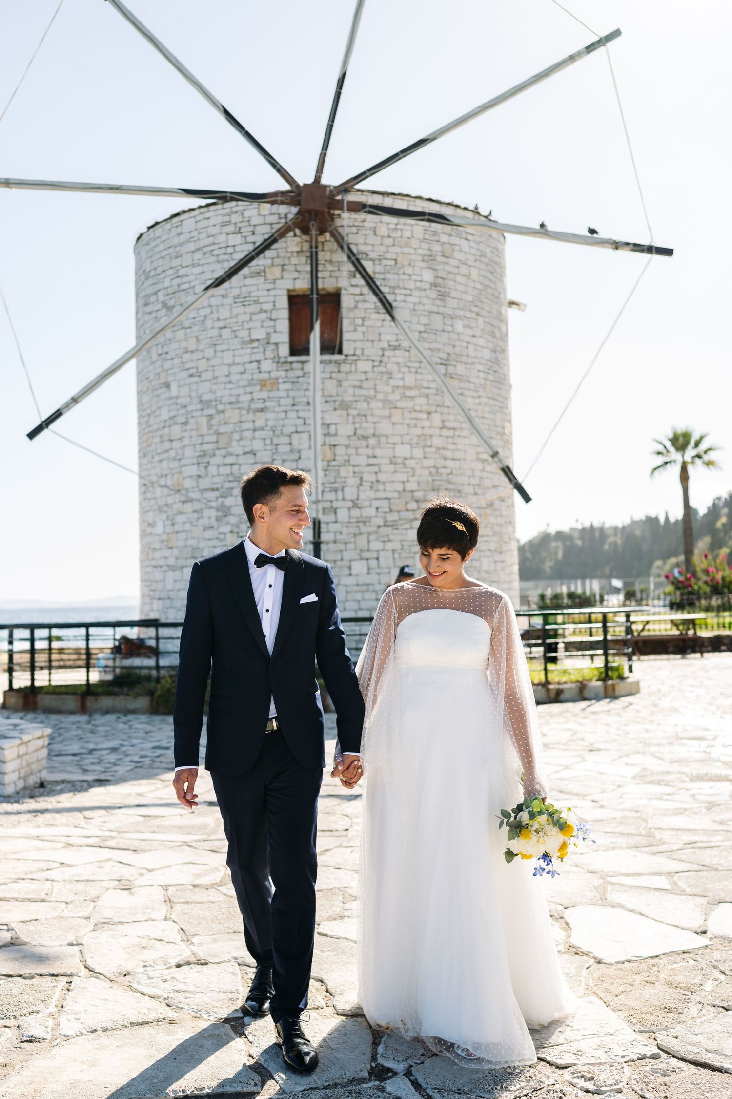 A romantic wedding photoshoot in front of a white stone windmill on a sunny day.