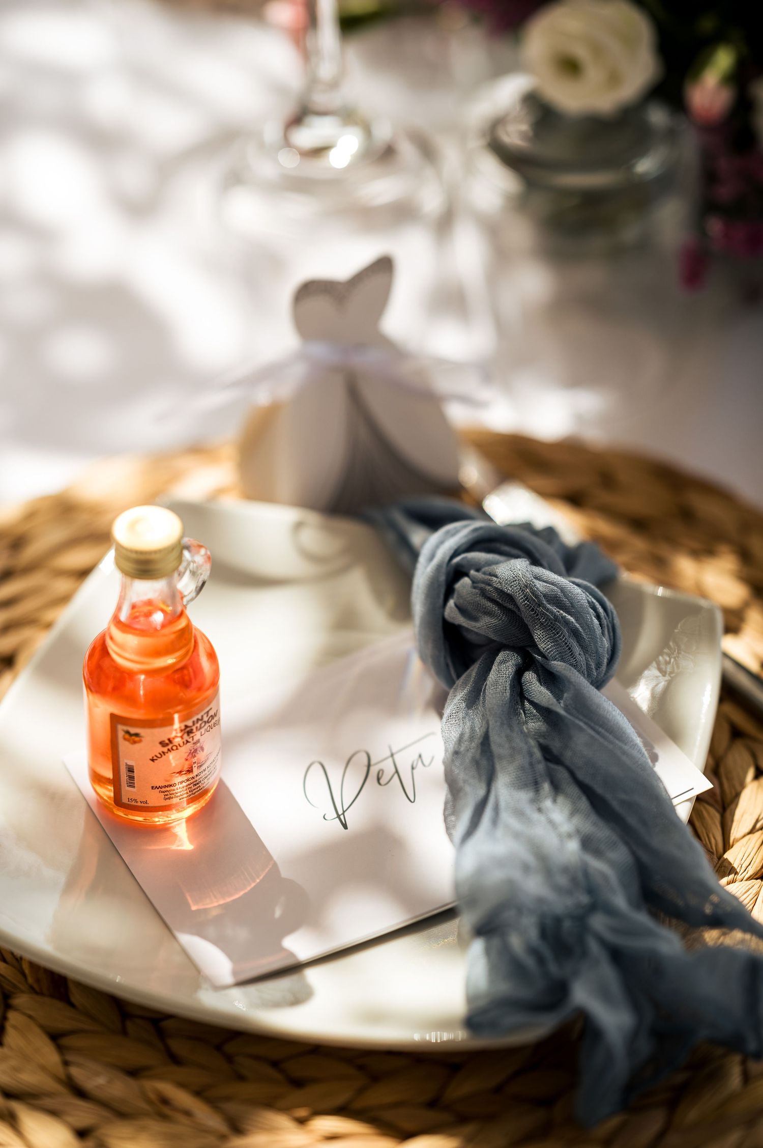 Wedding favor display with orange drink bottle and blue fabric on woven placemat.