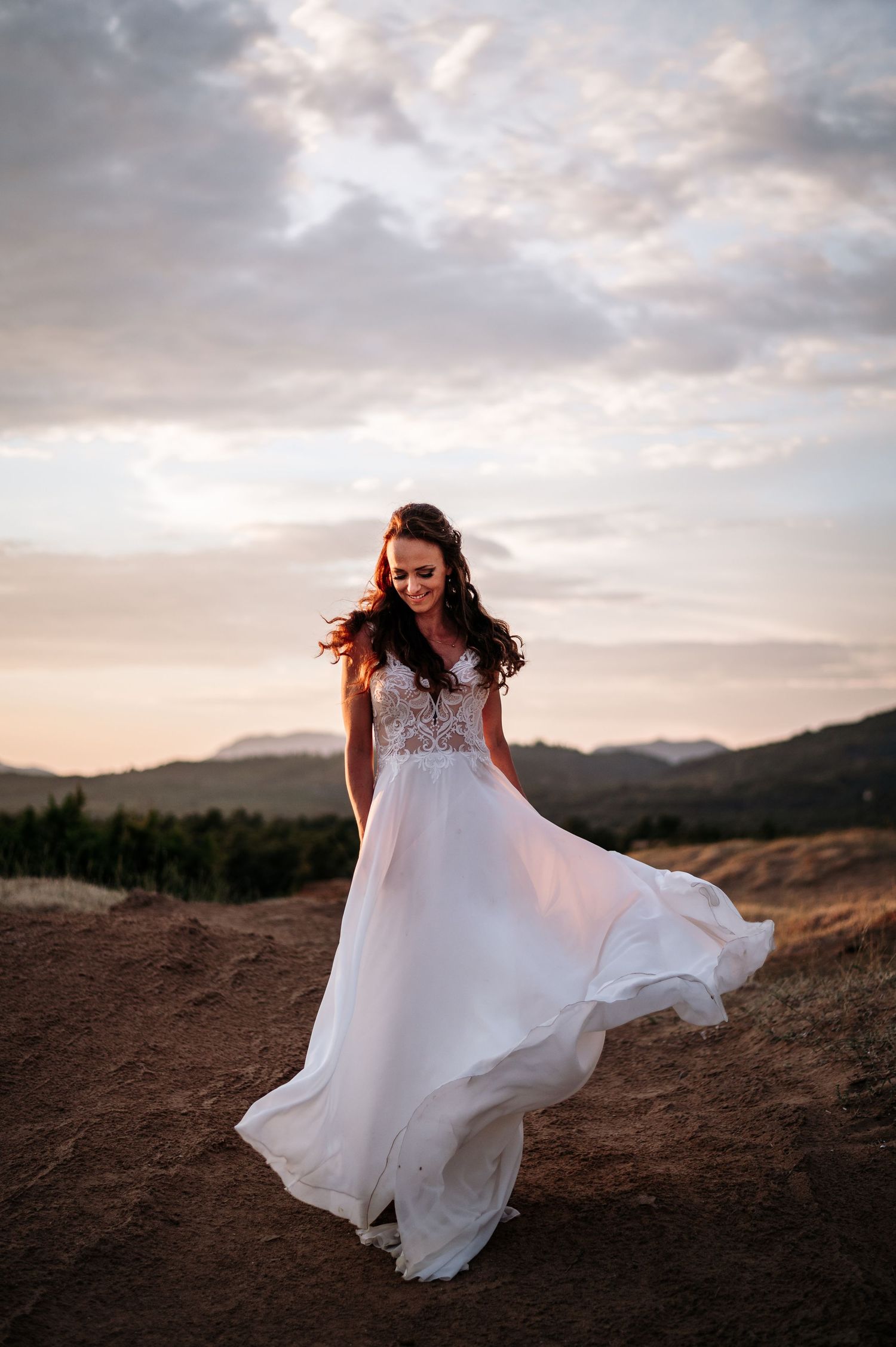Flowing white wedding dress twirls against sunset mountain landscape.