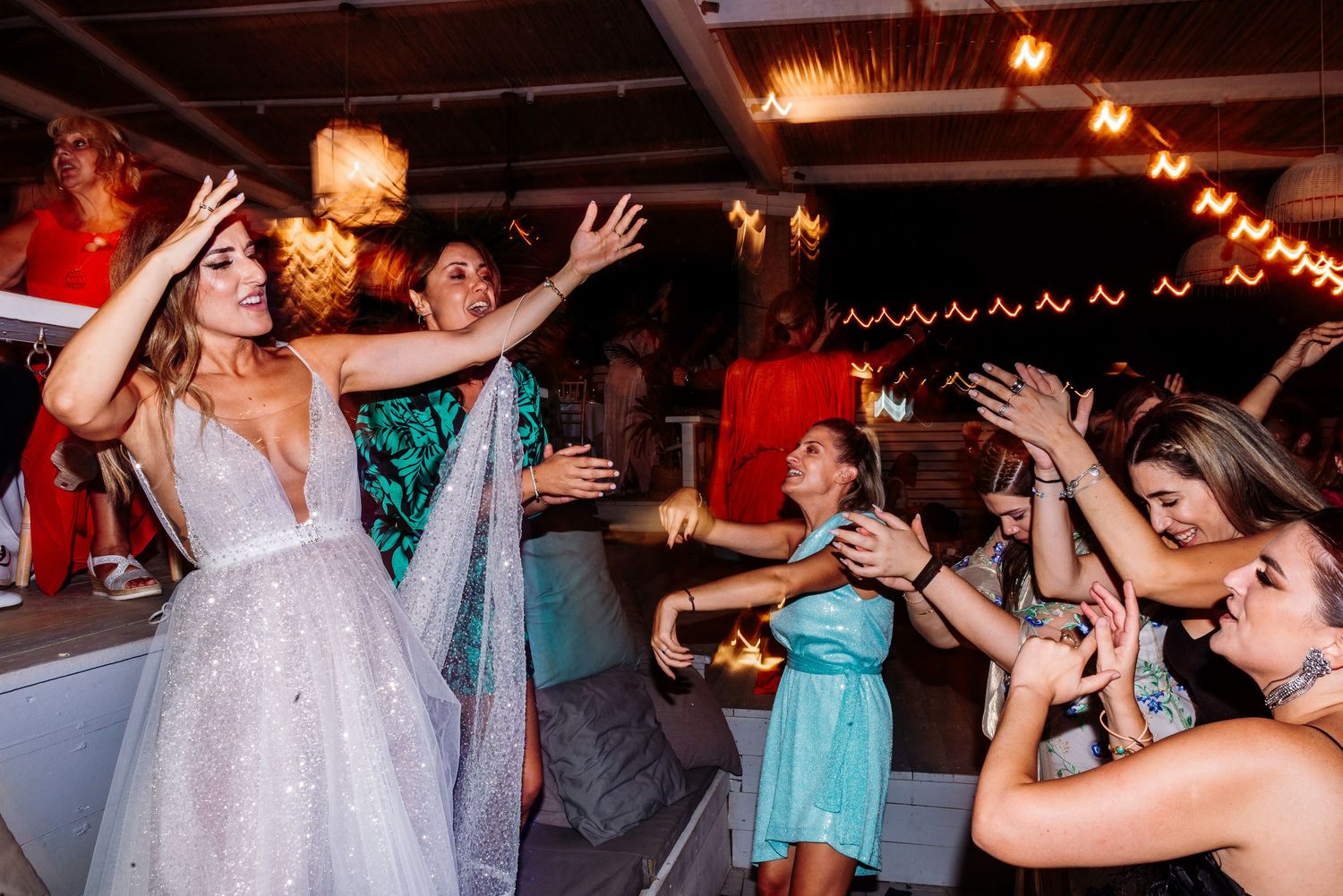 Wedding guests dancing enthusiastically under warm lighting at outdoor reception venue.