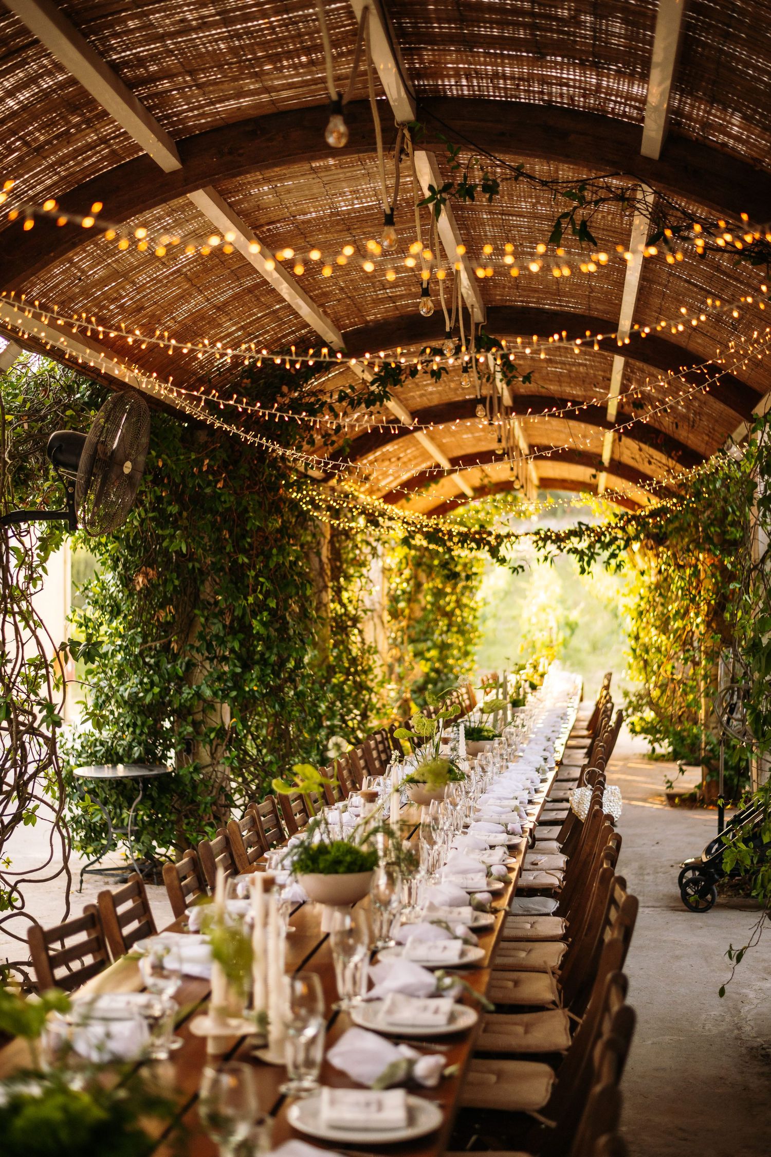 Rustic wedding reception venue with long tables set under string lights and wooden beams.