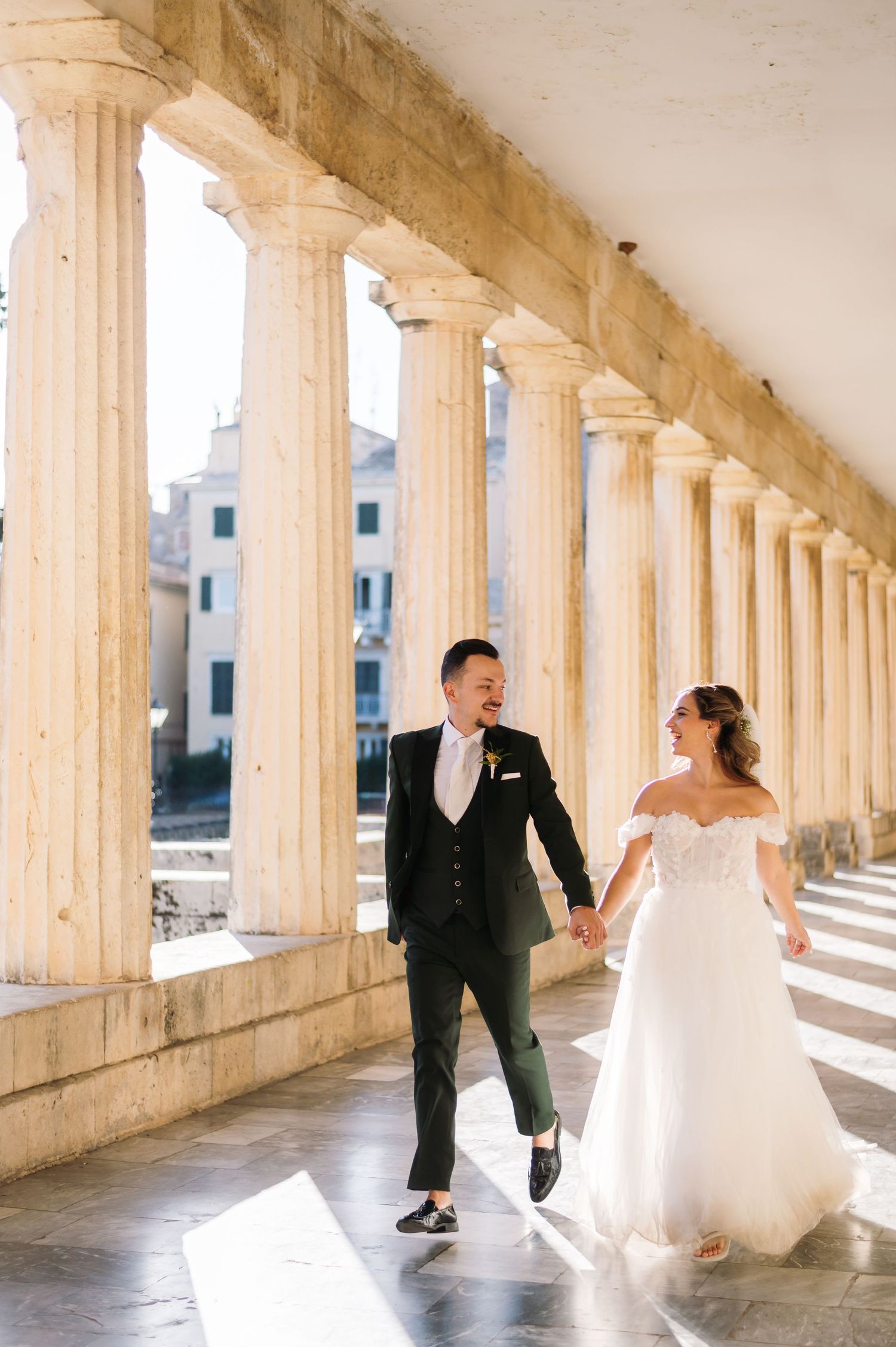 Playful wedding couple dances and twirls in a historic colonnade with repeating pillars.