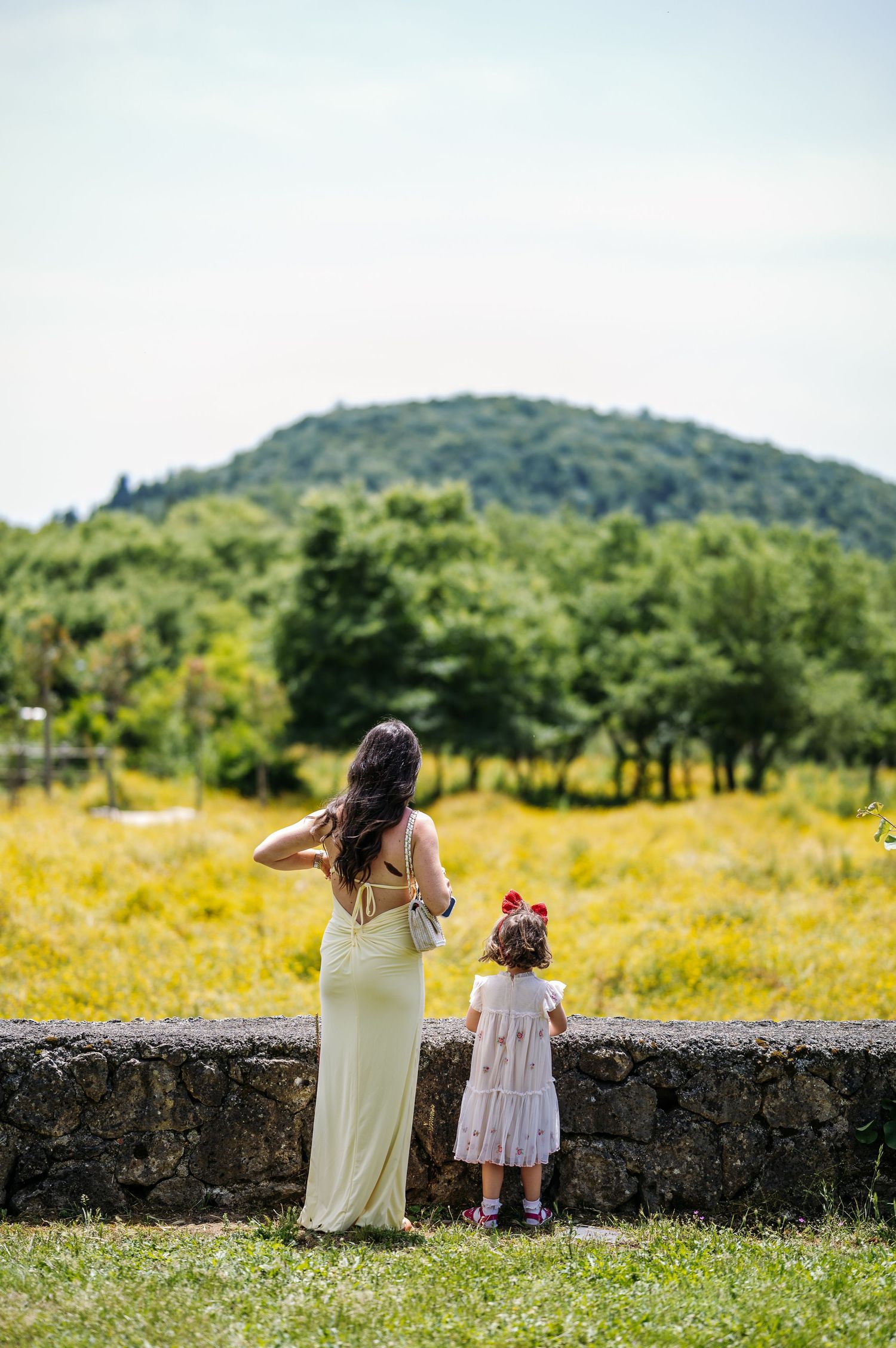 Two figures gaze at scenic mountain views while sitting on stone wall.