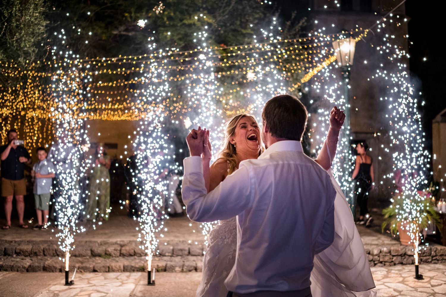 Couple dancing under sparklers and string lights during evening wedding celebration.