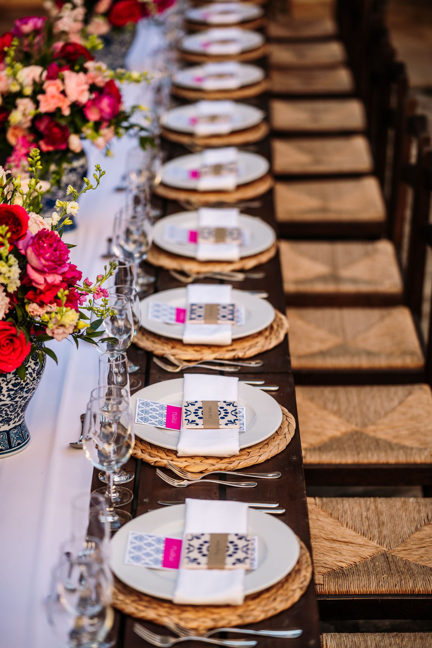 Elegant table setting with gold chargers, pink floral centerpieces, and white linens at a formal event.