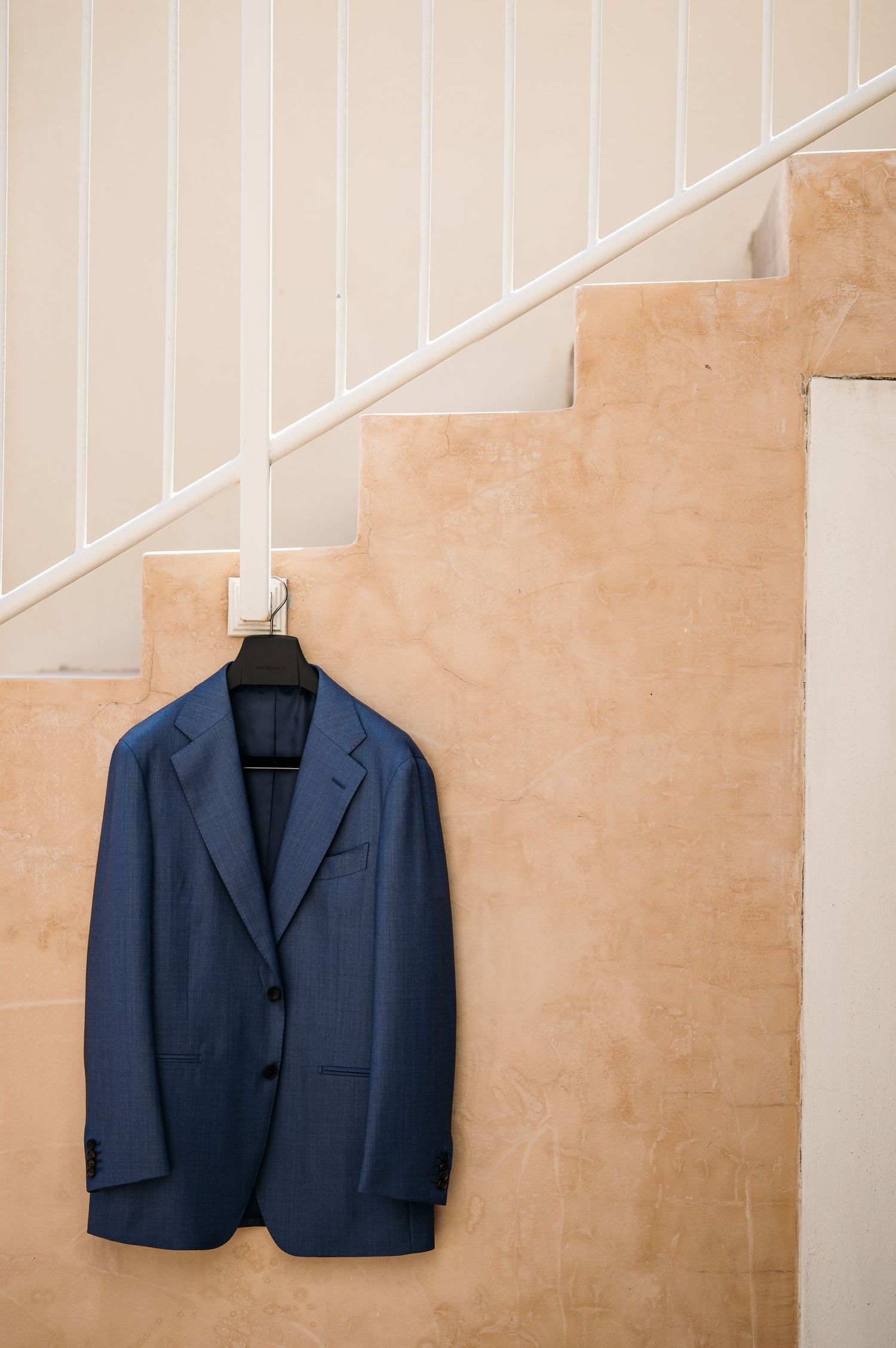 Navy blue suit jacket hanging on staircase railing against beige wall.