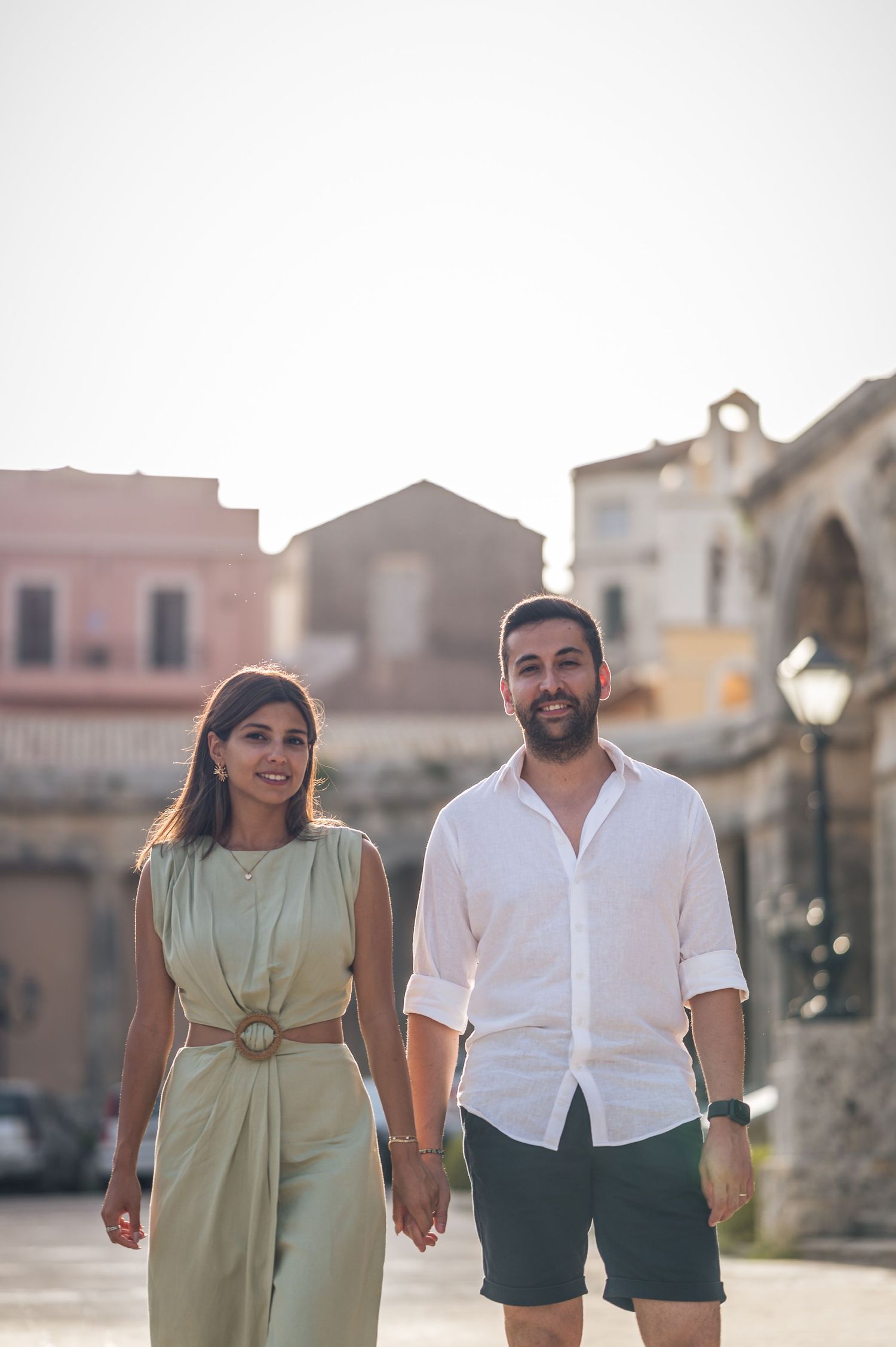 A summer evening stroll through a Mediterranean town square with historic buildings in the background.