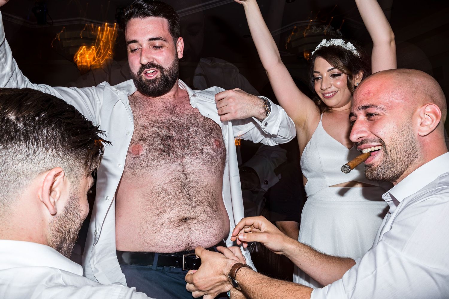 Lively group of wedding guests dancing and having fun in a dimly lit reception venue.