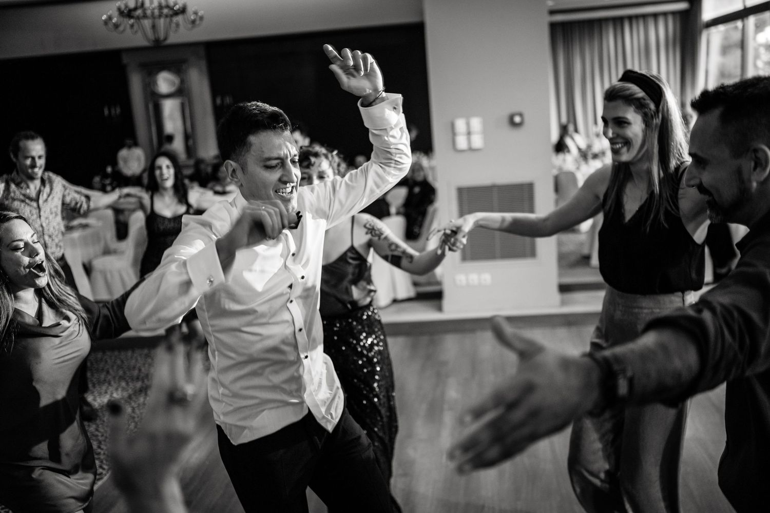 Wedding guests dance energetically on a dimly lit dance floor during a reception celebration.