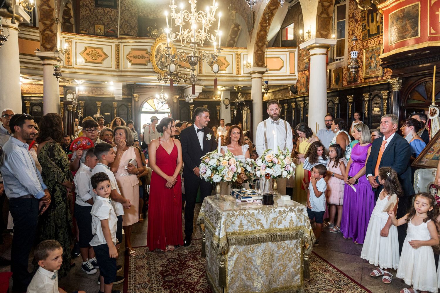 Wedding guests gather in an ornate reception hall with elegant chandeliers and decorative details.