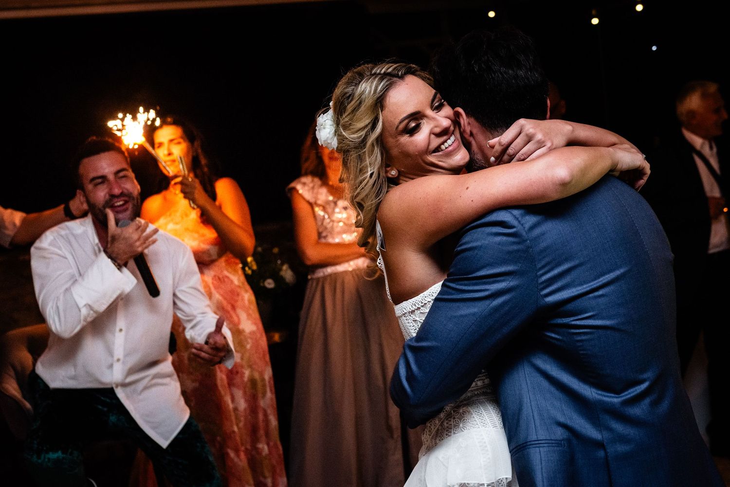 Couples embrace while dancing under warm ambient lighting at evening celebration.