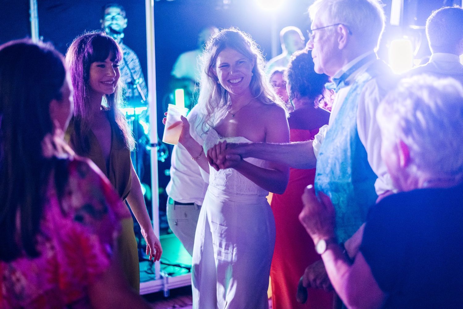 Wedding party dancing under blue lighting on crowded dance floor.