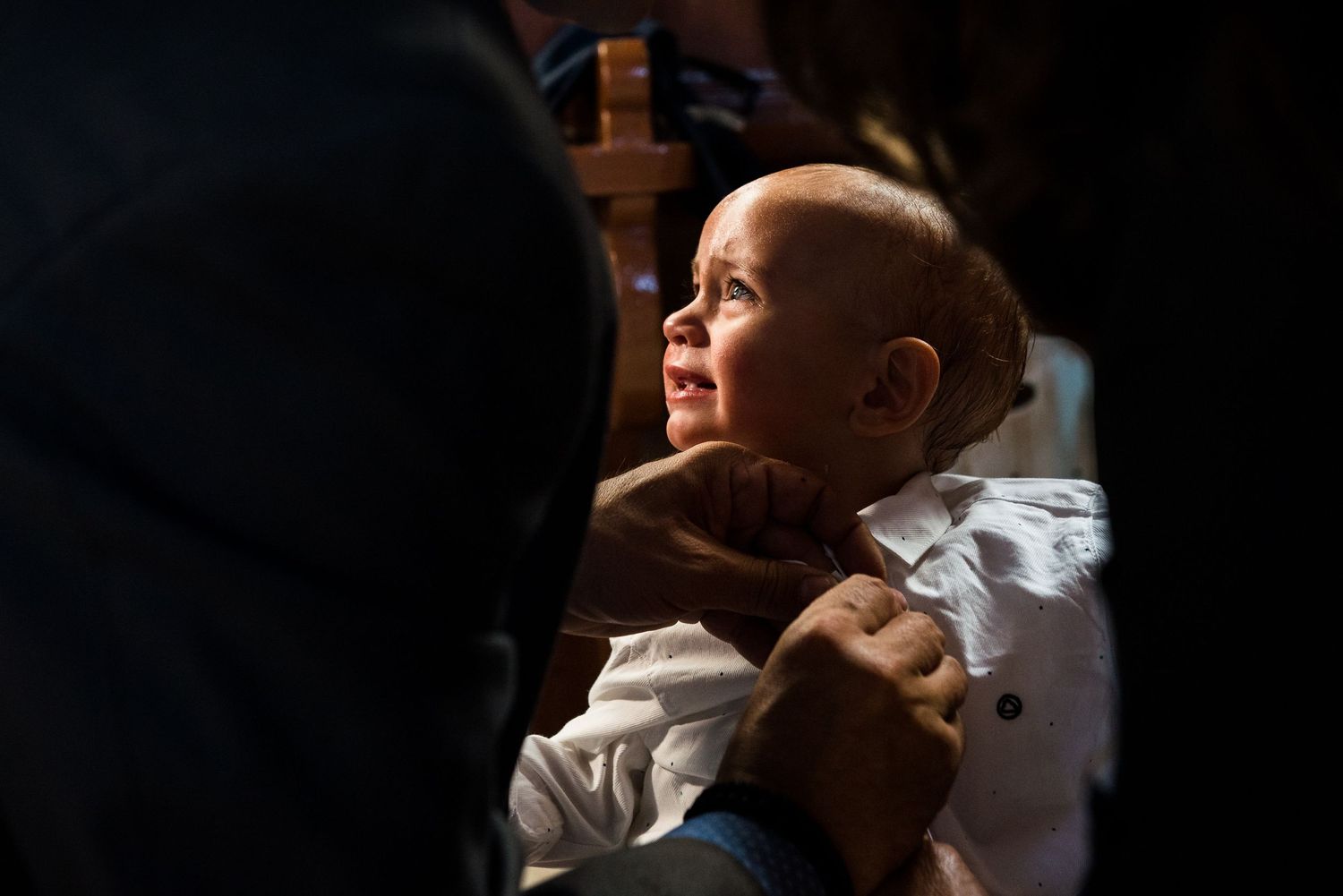 A baby in white clothing being held during a dimly lit baptism ceremony.