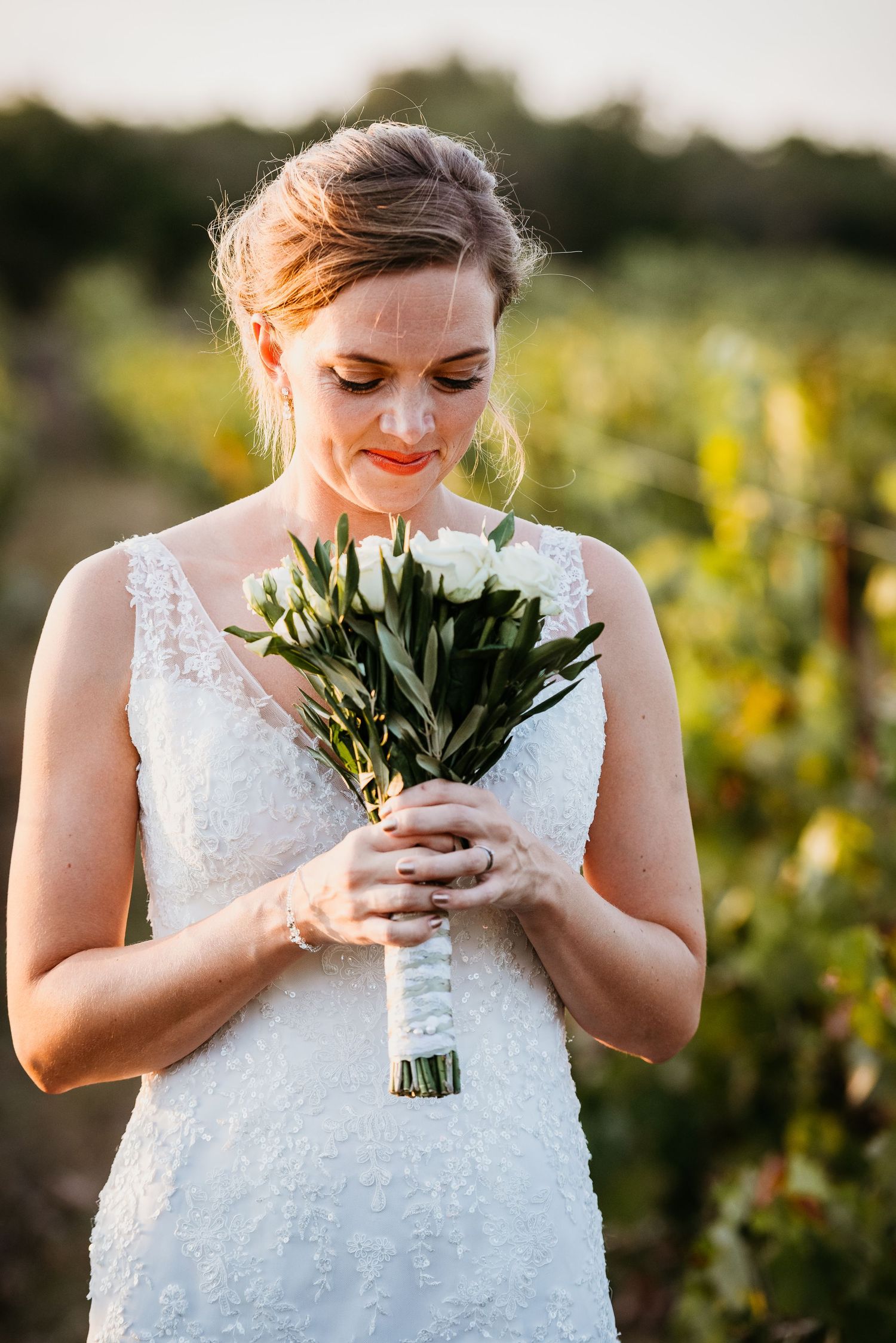 White bridal bouquet held against lace wedding dress in golden sunlight.