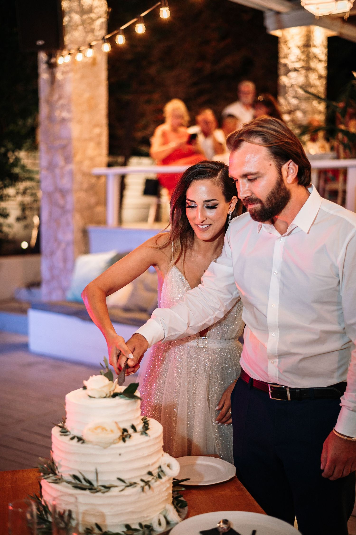 Couple cutting their white wedding cake decorated with greenery.