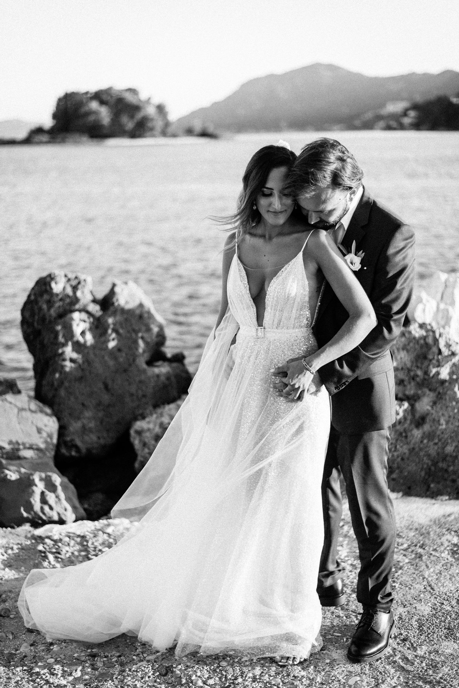 Romantic coastal wedding photos with flowing white dress against rocky shoreline.