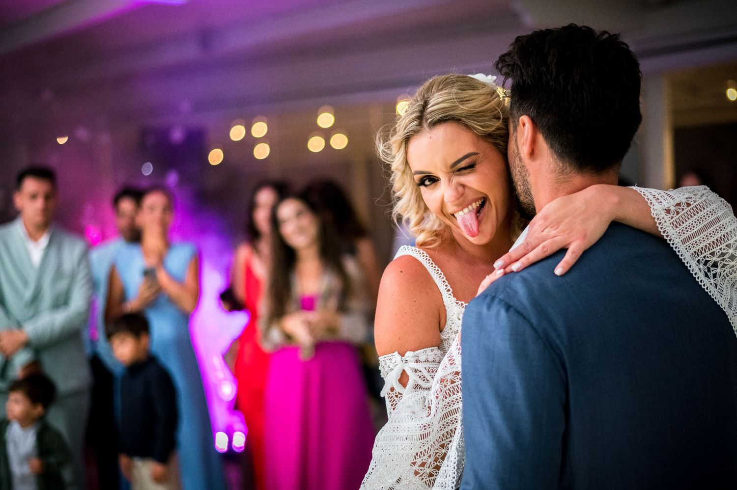 Wedding couple dances under purple lighting at evening reception.