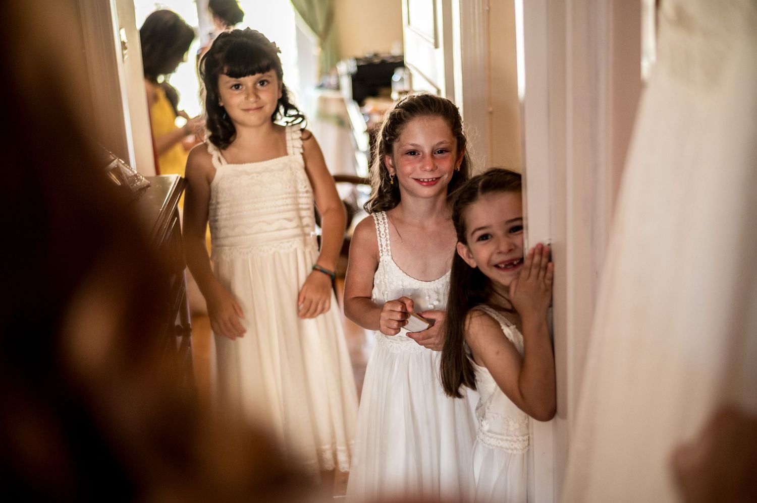 Young attendants in white dresses peek through a doorway.