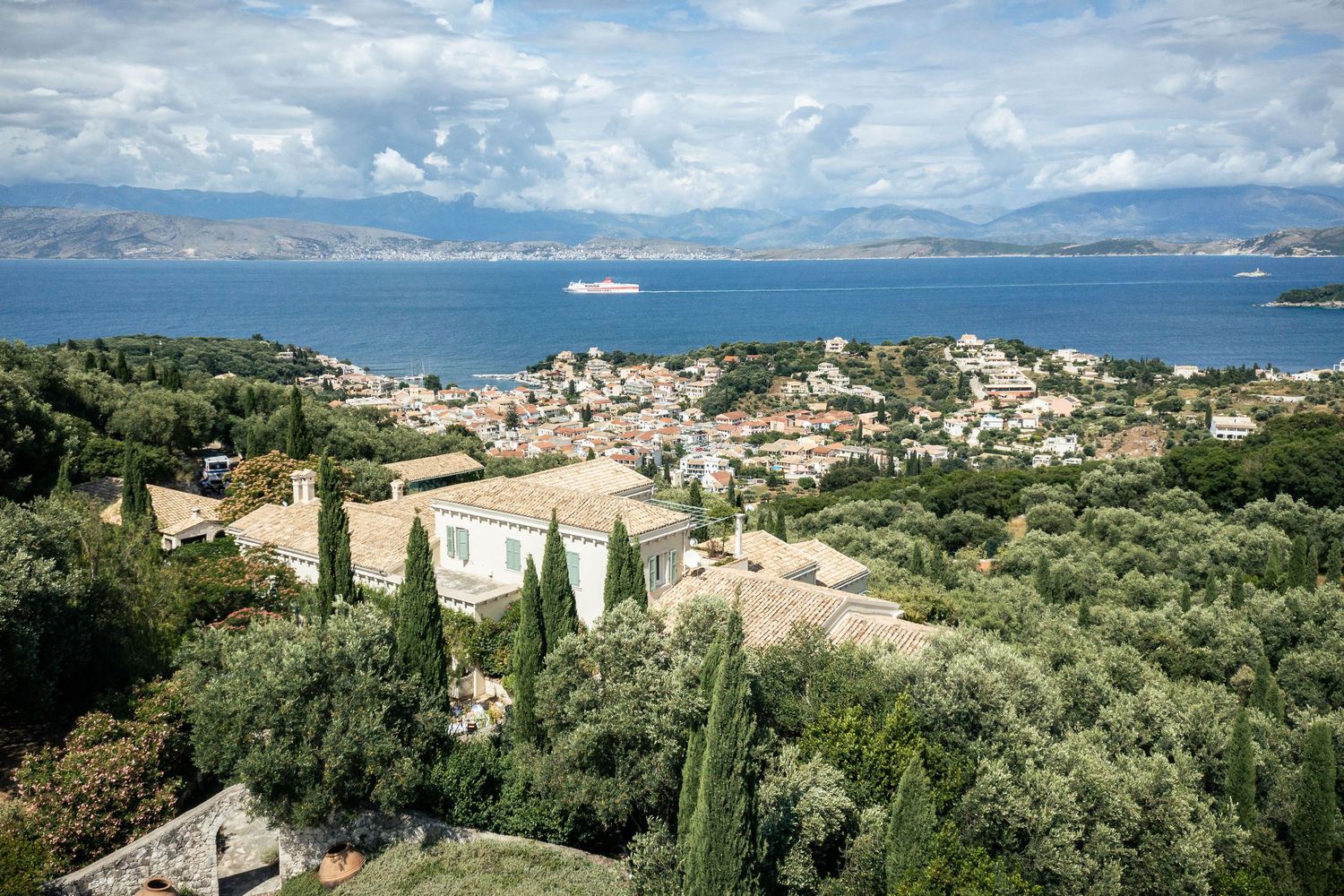 Panoramic coastal landscape view of Mediterranean buildings and sea under cloudy skies in Kassiopi, Corfu.