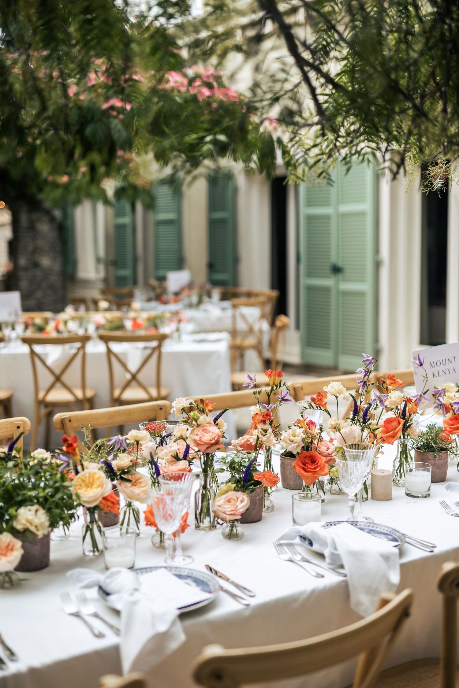 Long banquet tables decorated with coral and peach floral centerpieces at an outdoor wedding reception.