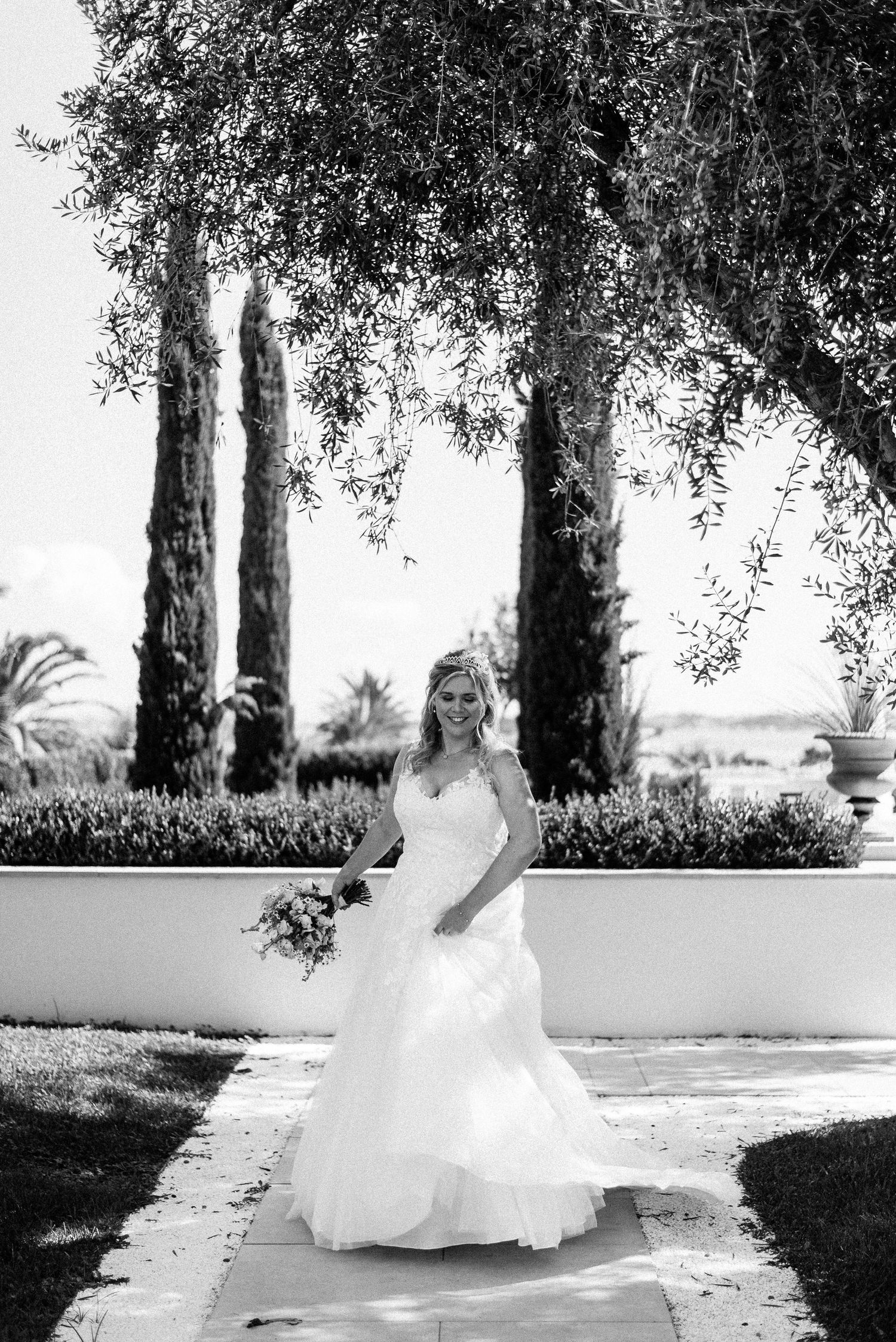 White wedding dress photographed in a garden setting with olive trees.