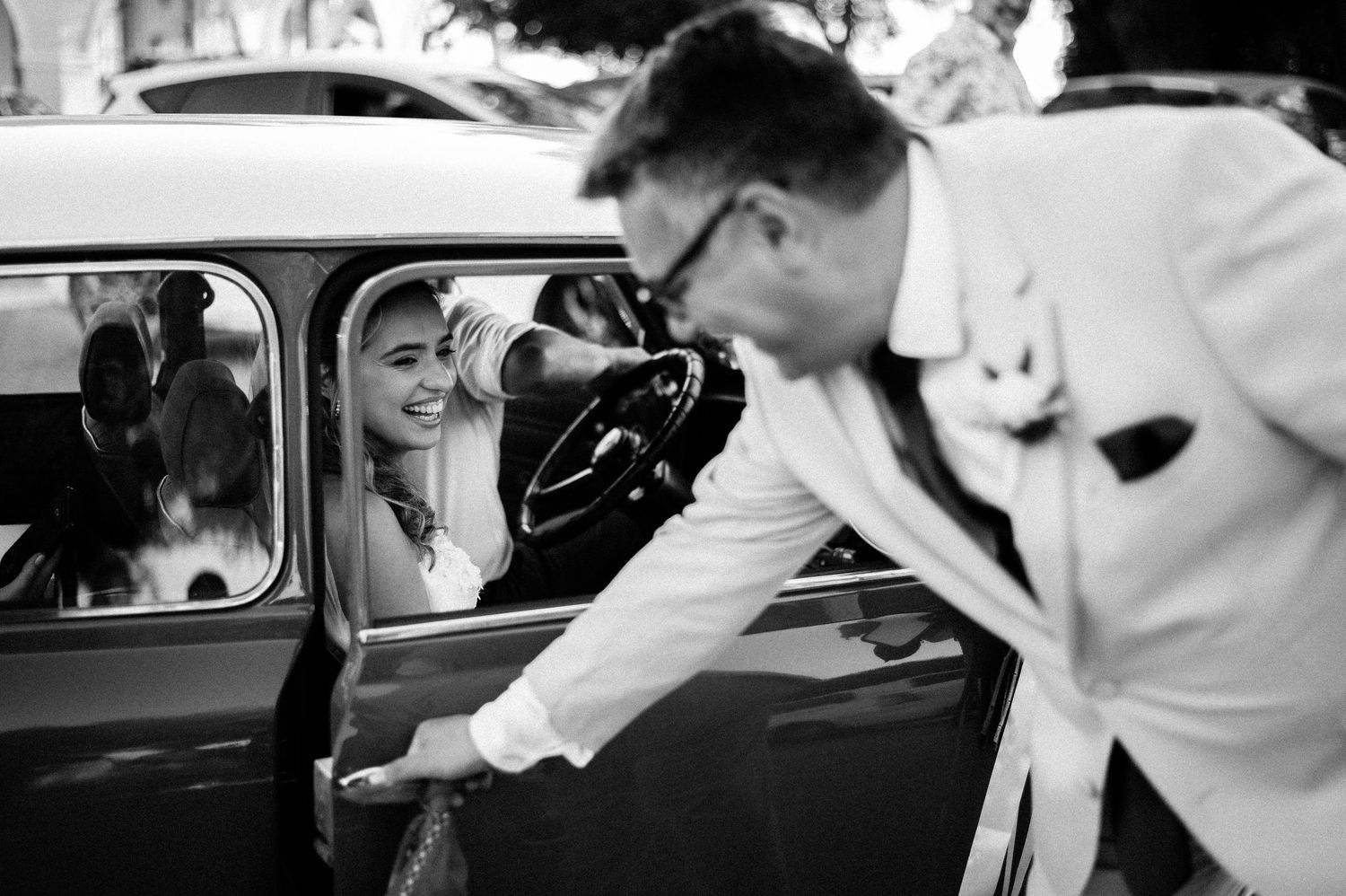 Black and white photographs capturing intimate moments between newlyweds near vintage cars.