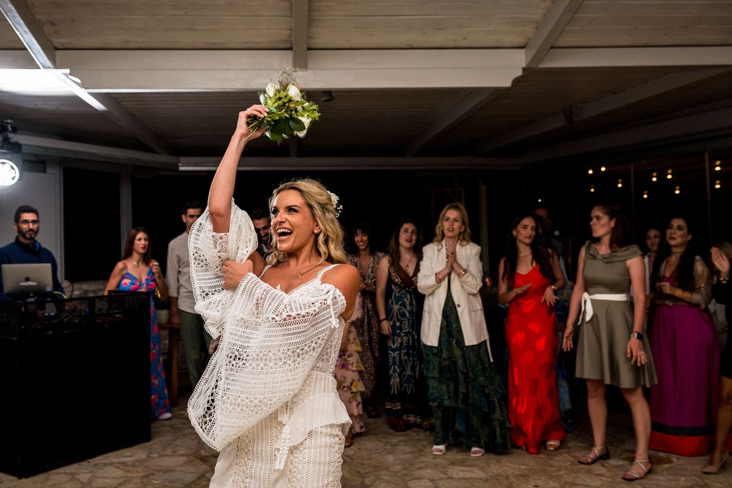 Wedding reception venue with guests dancing under string lights and white ceiling decor.