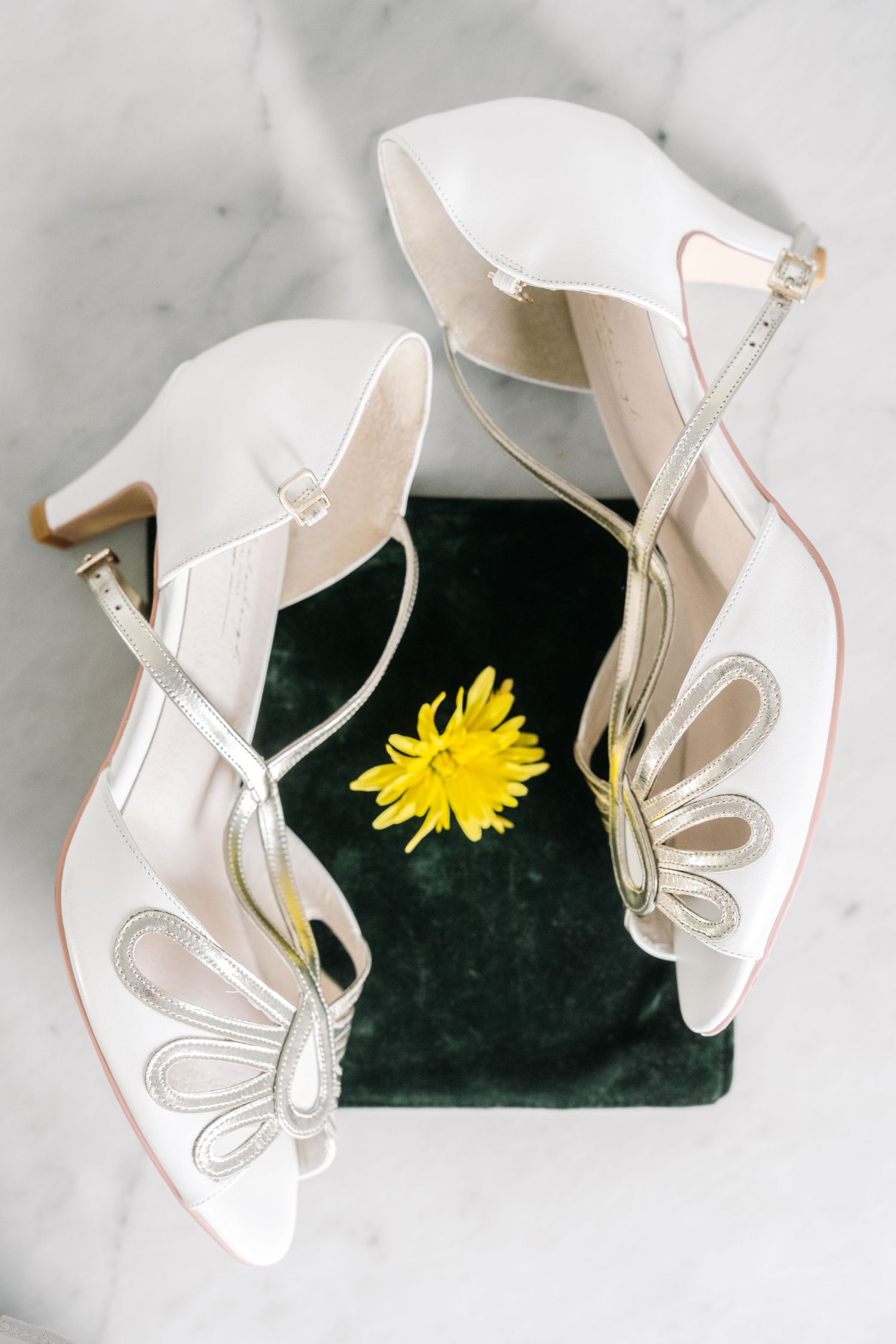 White bridal shoes with delicate butterfly details photographed against a dark background with yellow flowers.