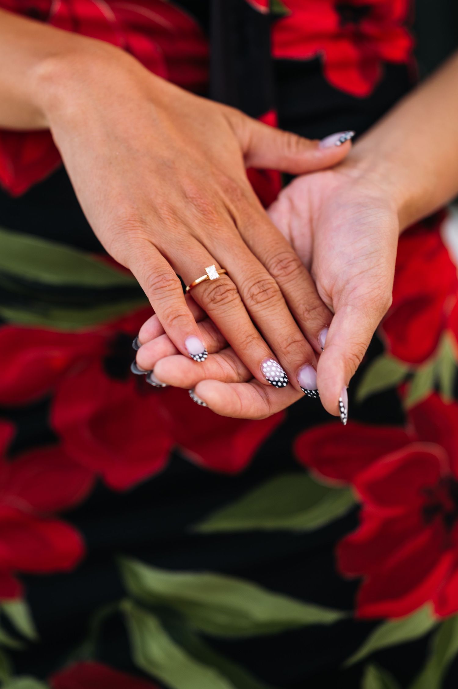 Close-up shots of engagement rings on hands with red floral backdrop.