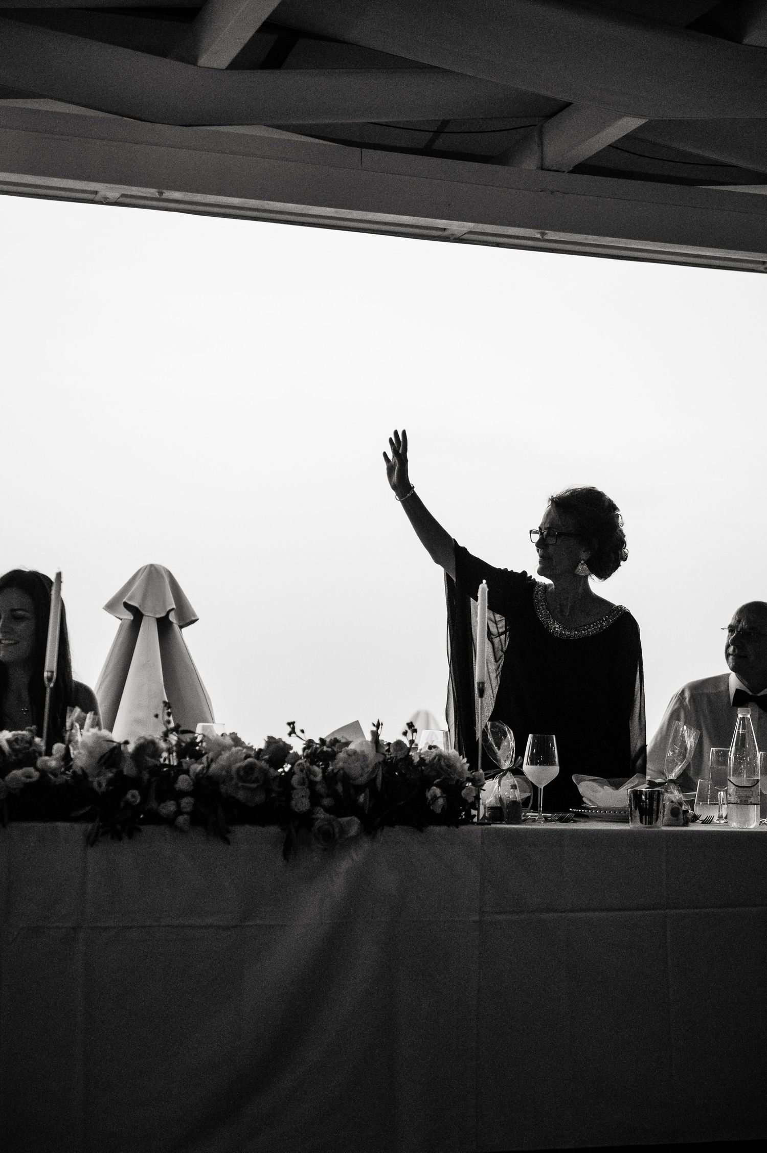 Wedding guests raise their hands in celebration during an outdoor reception silhouetted against the sky.