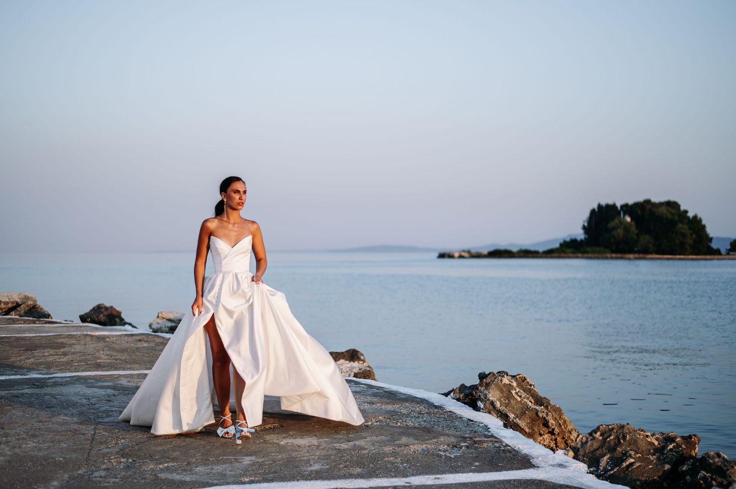 Seaside bridal portraits featuring elegant white wedding gown against blue water.