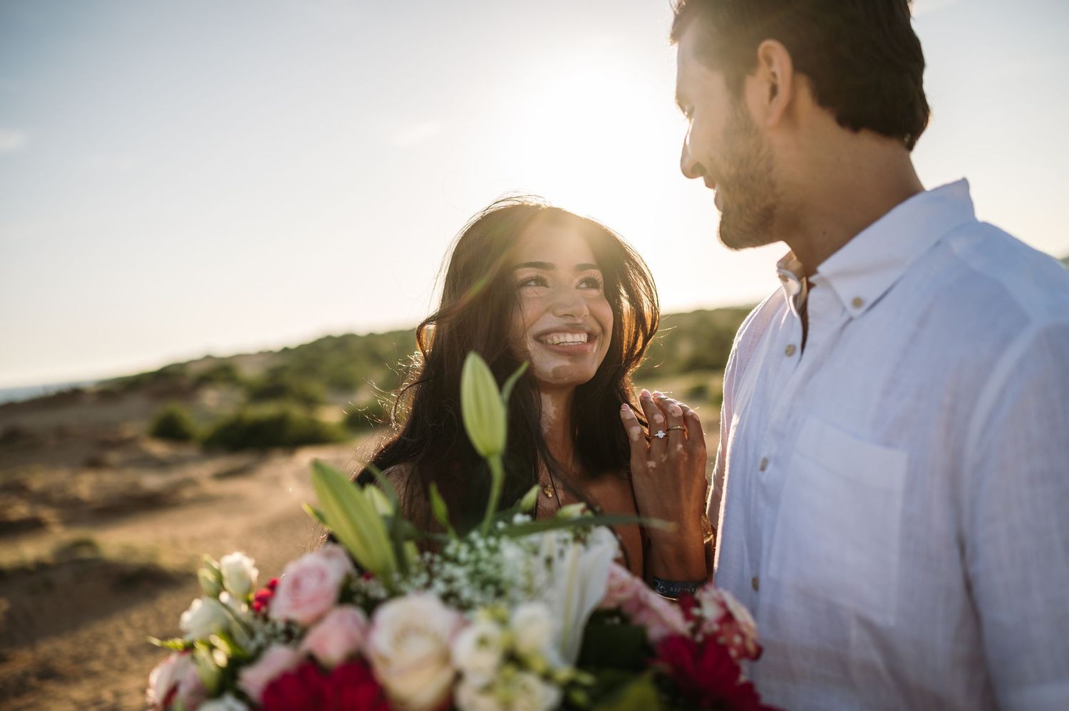 A couple sharing a joyful moment during a beach proposal with decorative elements.