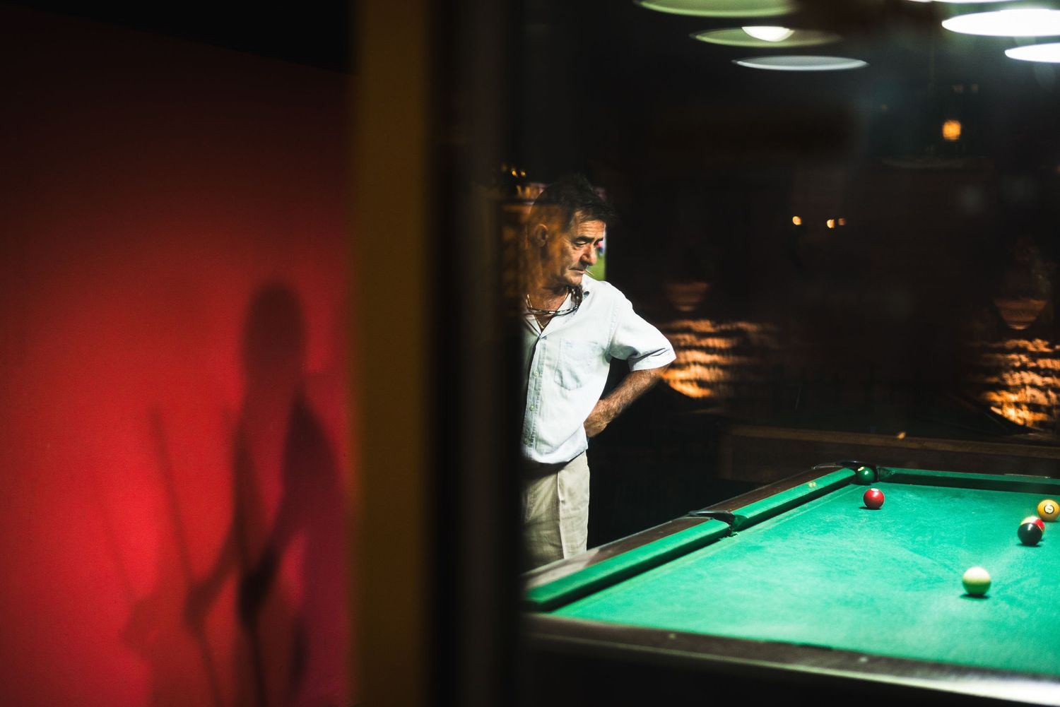 Moody interior of a pool hall with green table lighting and dark atmospheric shadows.