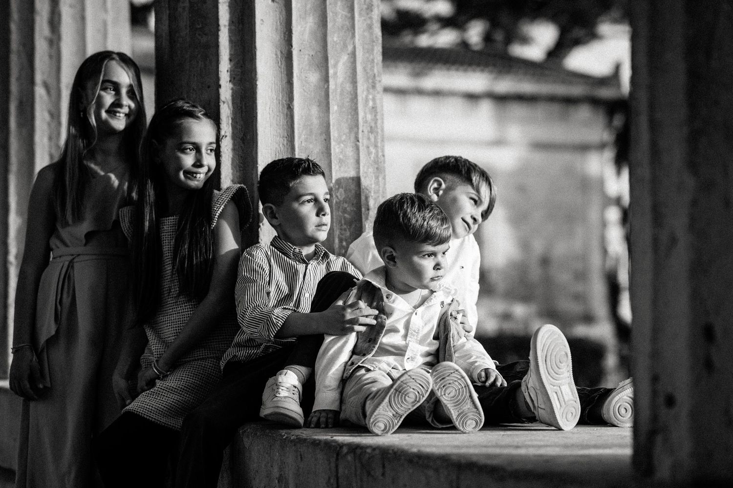 Black and white photo of children sitting together on a ledge near classical columns.