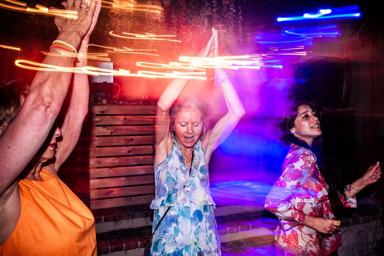 Colorful neon lights illuminate wedding guests dancing at a lively reception.