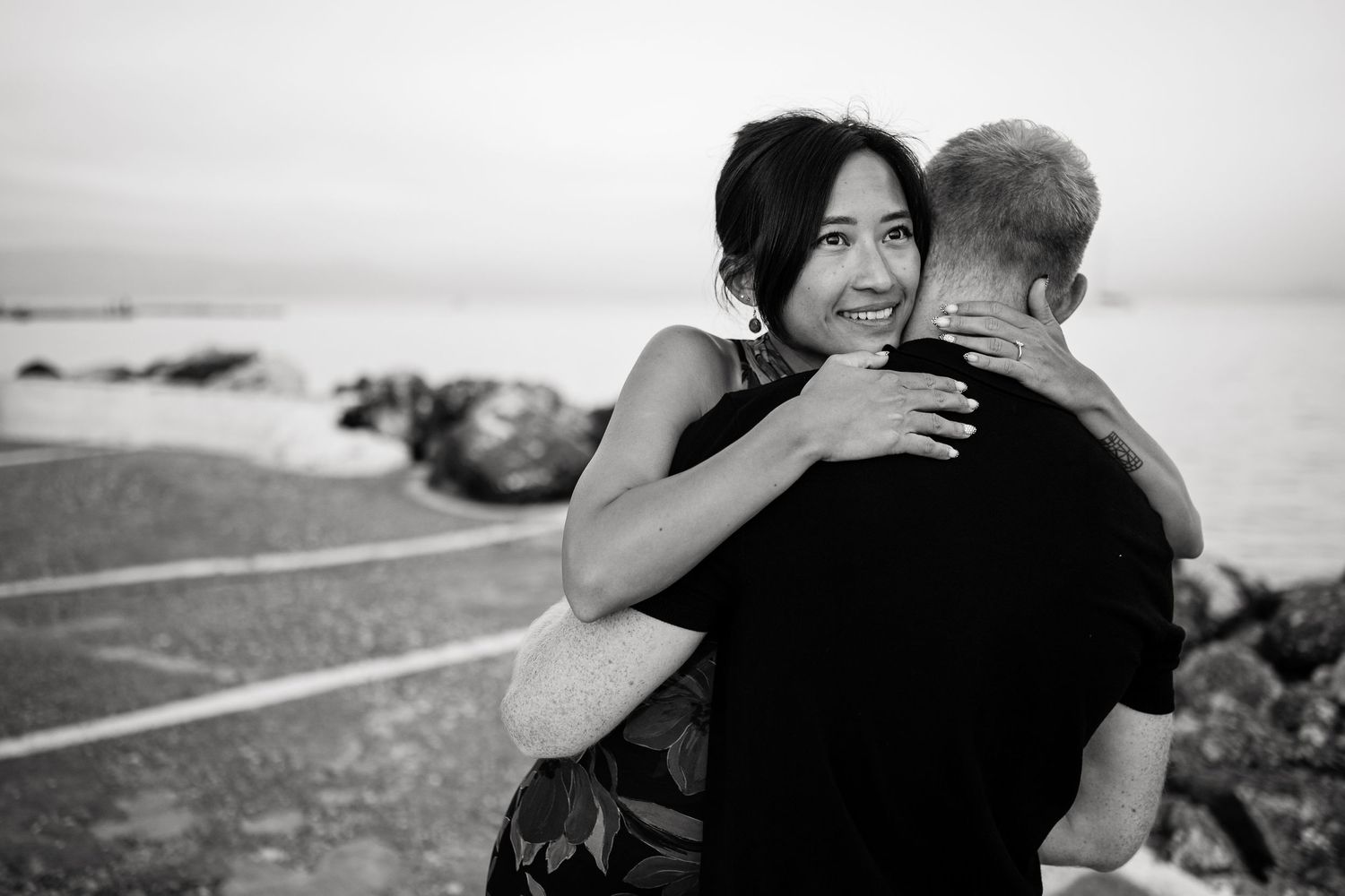 A black and white photo of a couple hugging by the seaside.