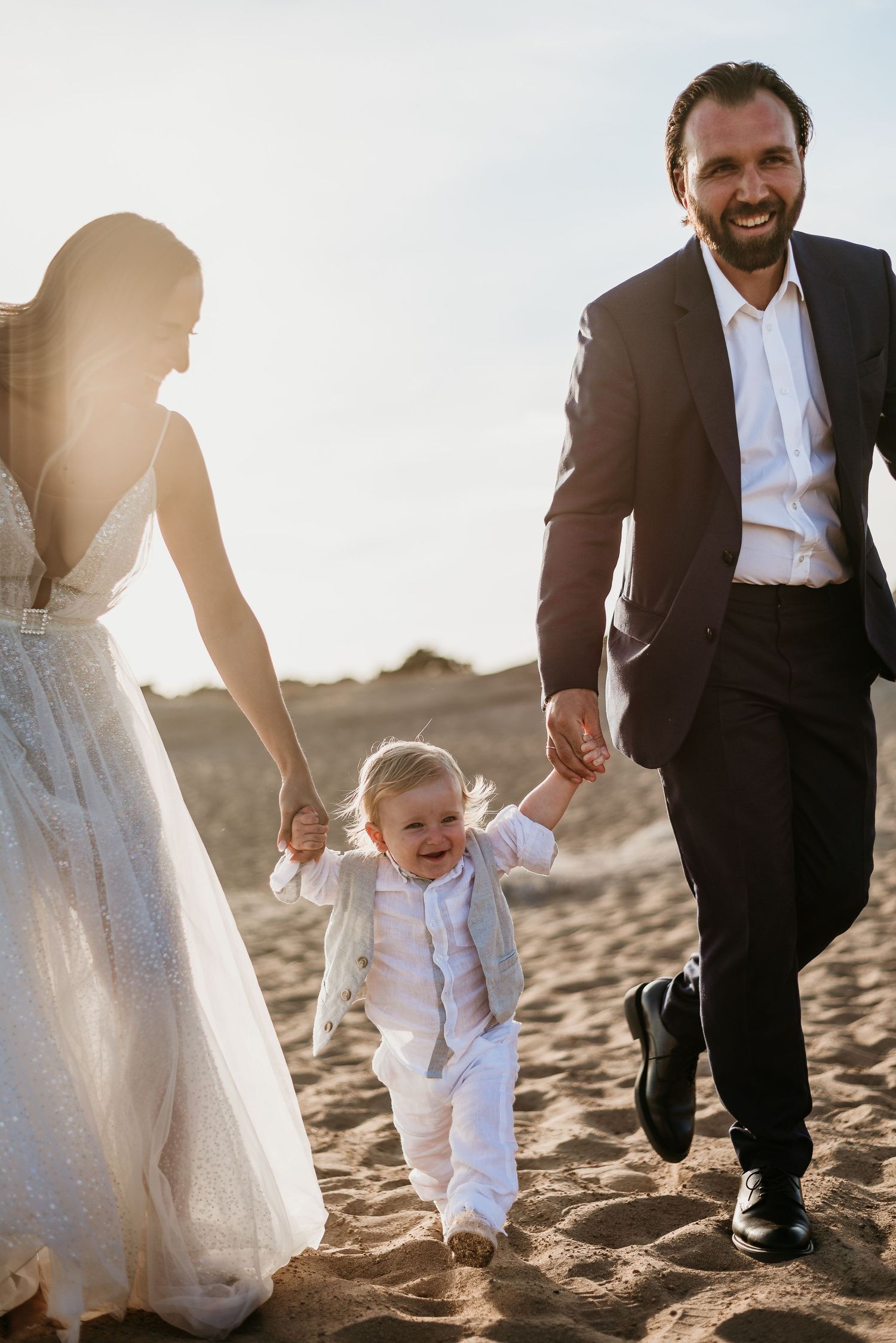 A couple and child walk together on sandy beach during golden hour.