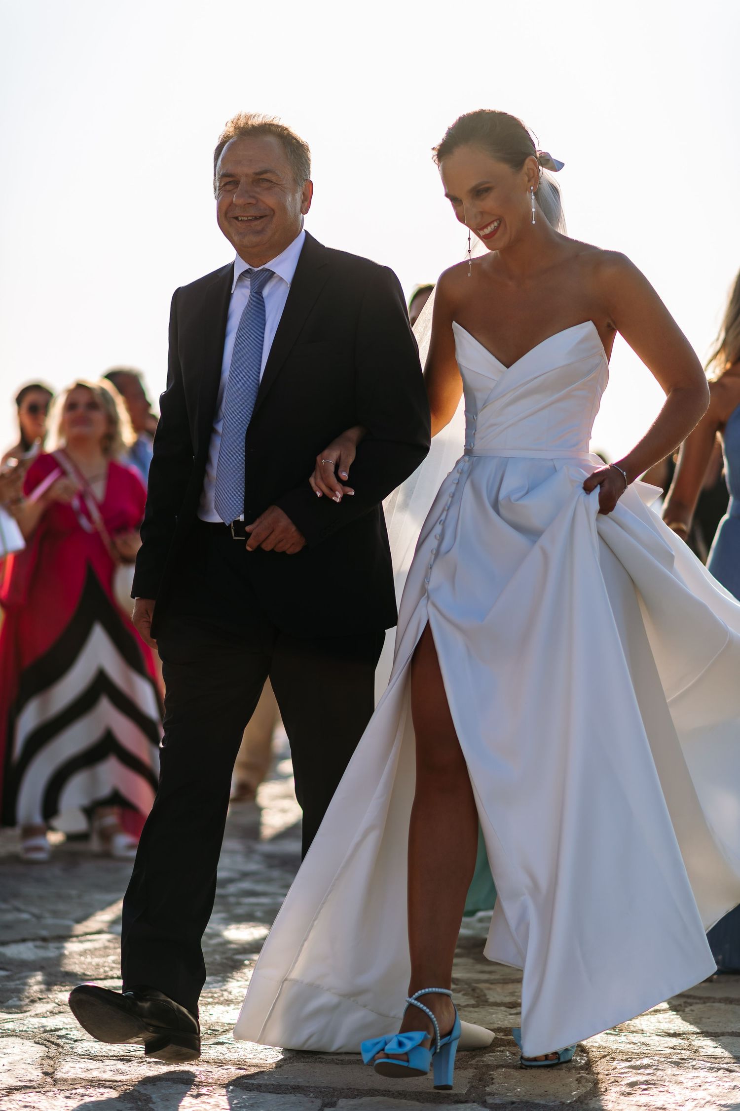 Wedding party walks along coastal path with bride wearing bright blue shoes.