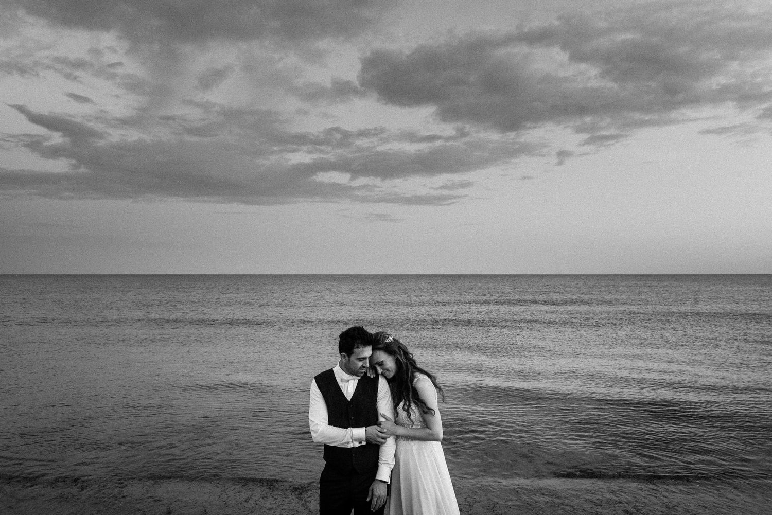 Wedding couple silhouetted against dramatic cloudy sky over ocean horizon.