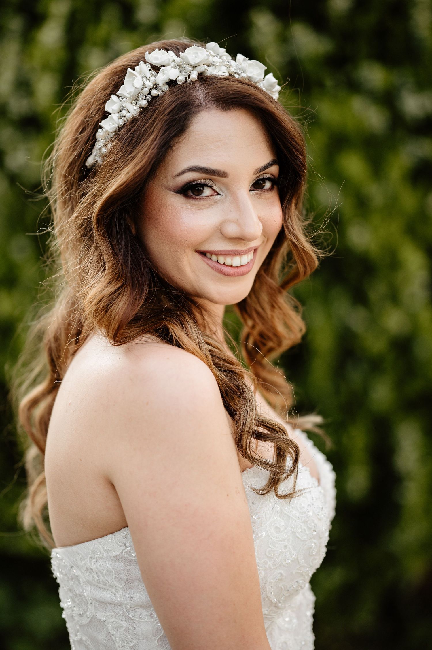 Beautiful bridal portrait with floral crown against lush green foliage background.