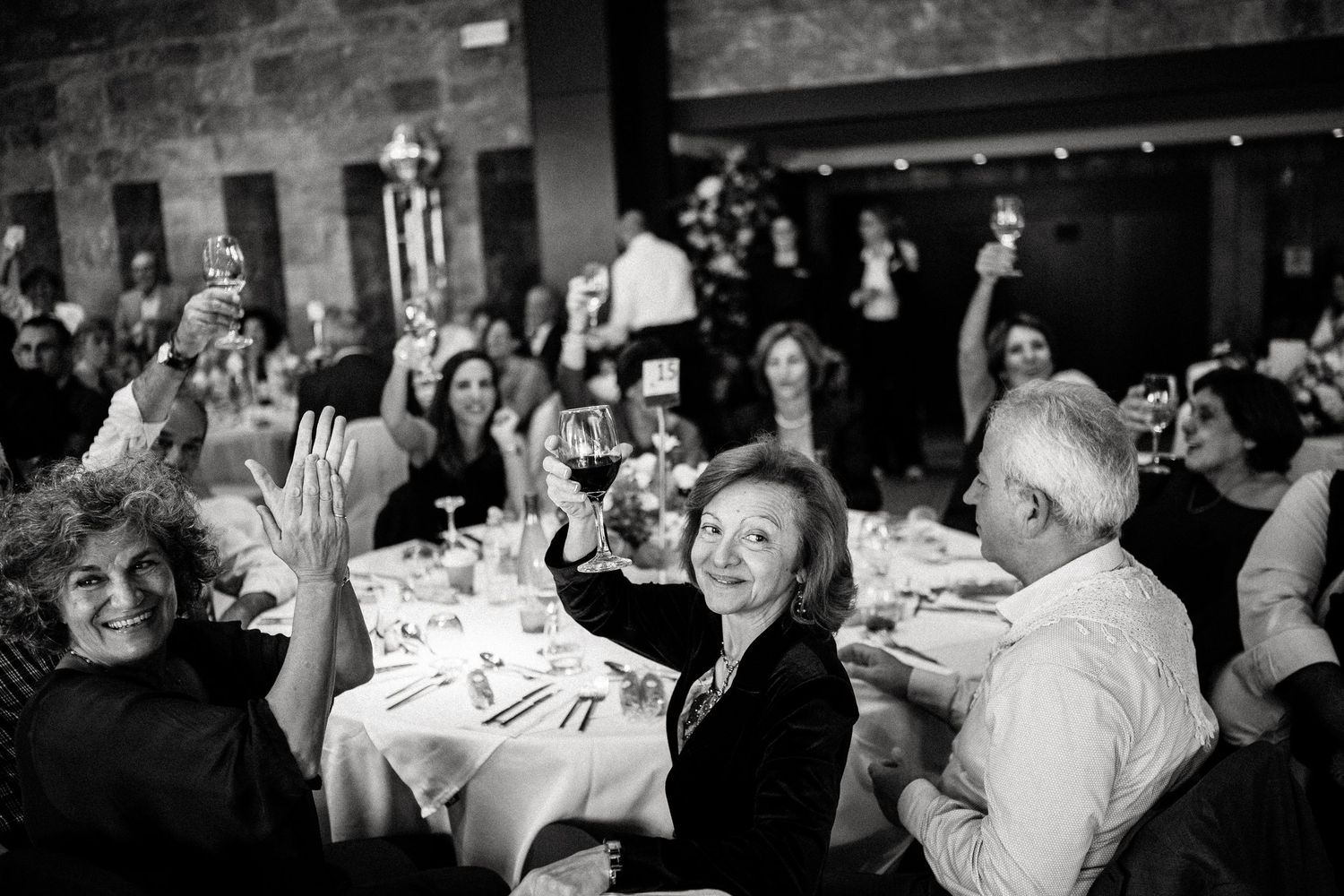 Wedding party and guests dance and celebrate in a rustic venue with exposed brick walls.