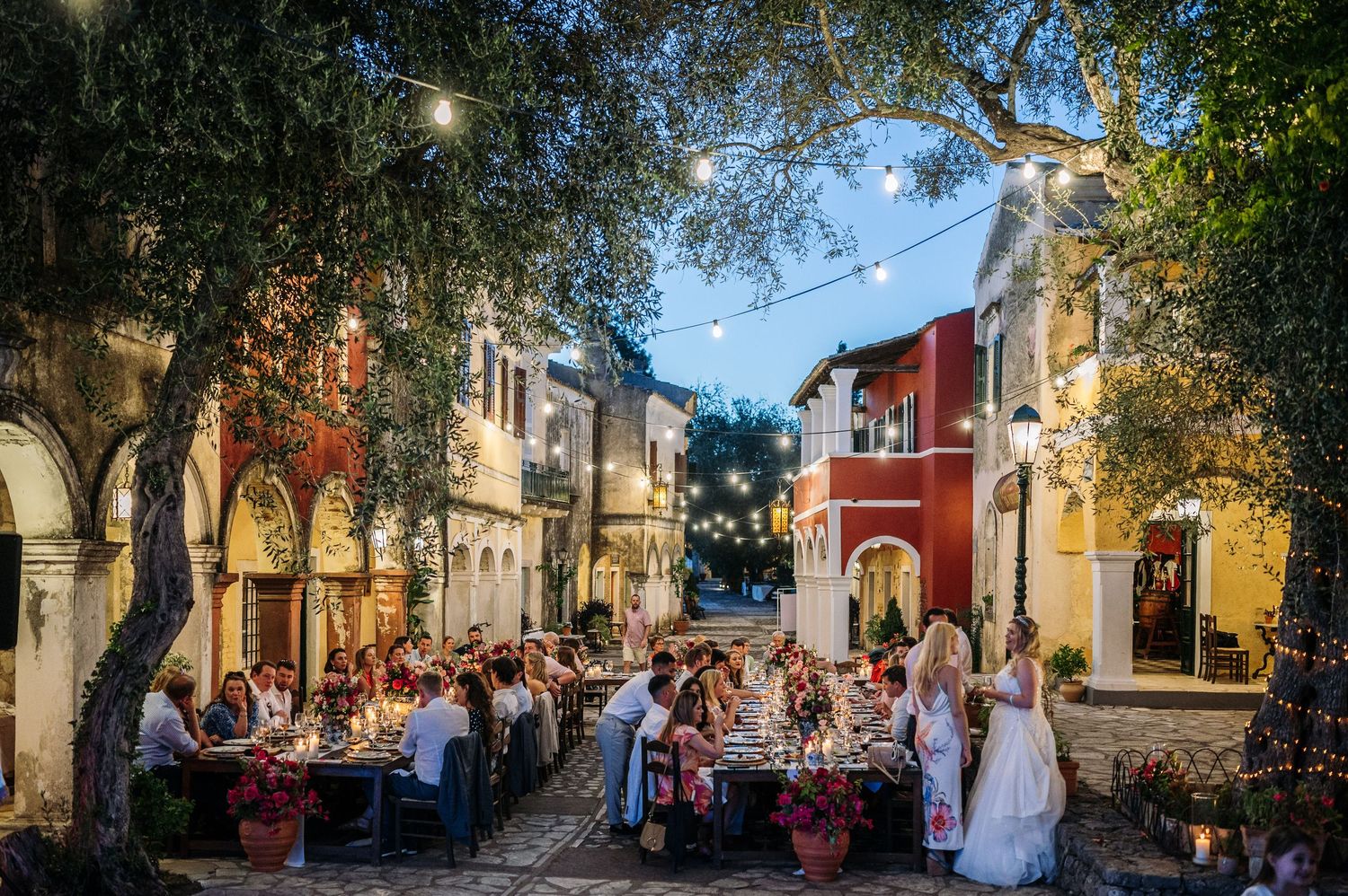 Sun-drenched Italian village street with outdoor dining tables and colorful buildings.