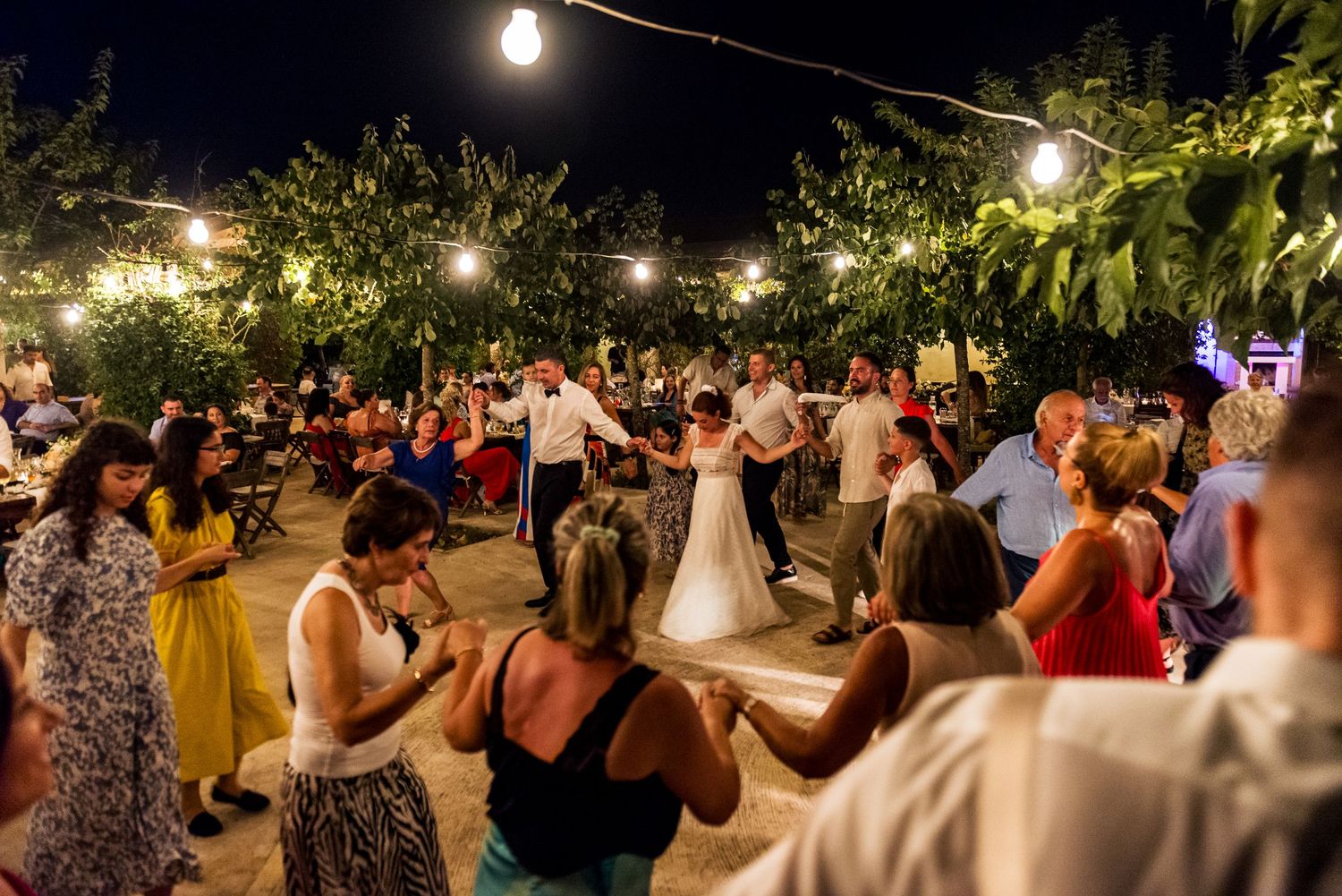 String lights illuminate an outdoor wedding reception space with dancing guests.
