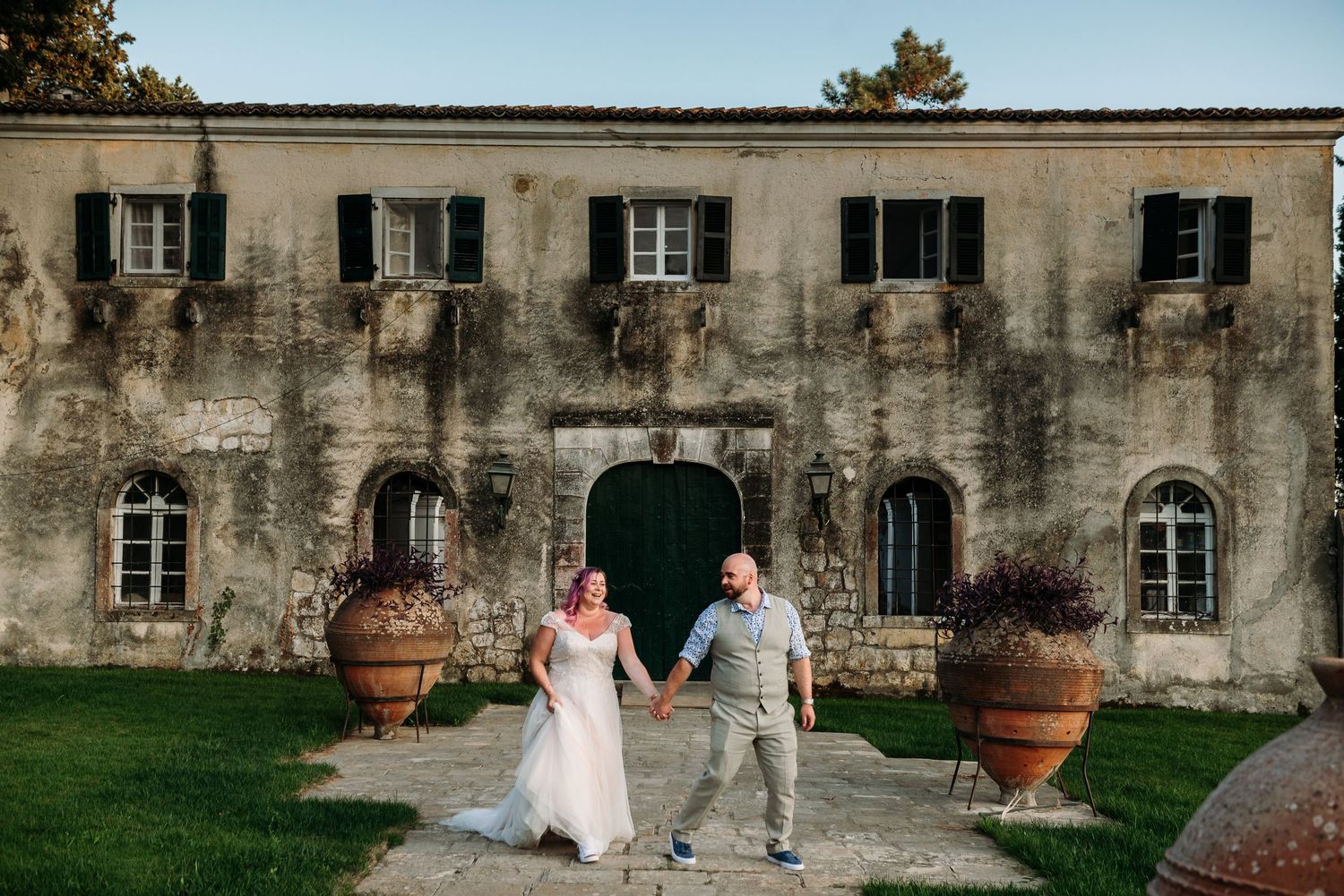 Couple poses in front of historic stone building with large terracotta planters.